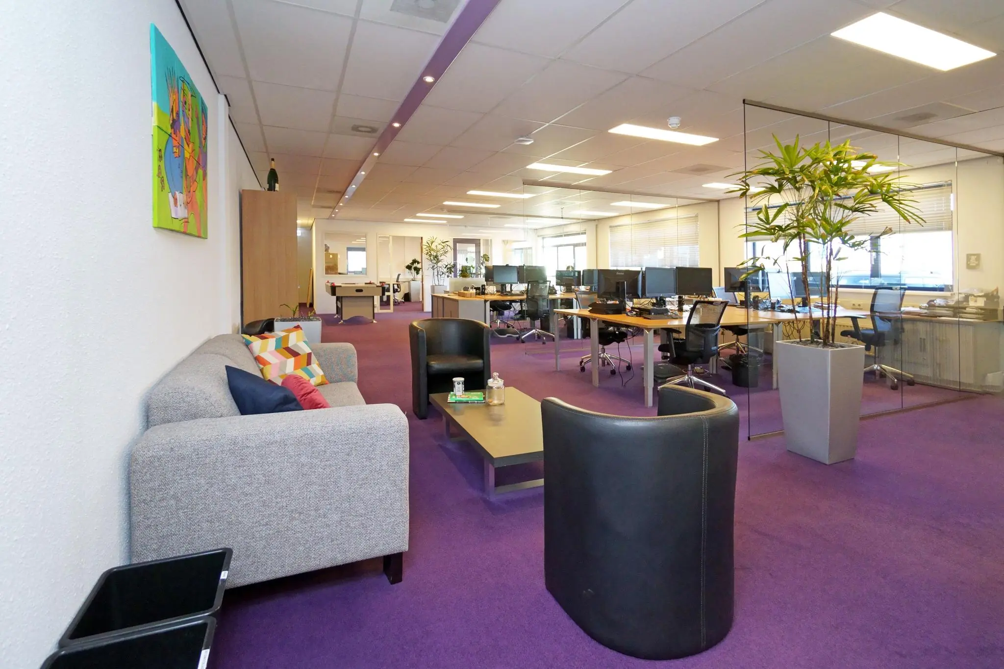 Modern kantoorinterieur aan de Zuiderweg met paarse vloerbedekking, open werkplekken en een zithoek met bank en stoelen.