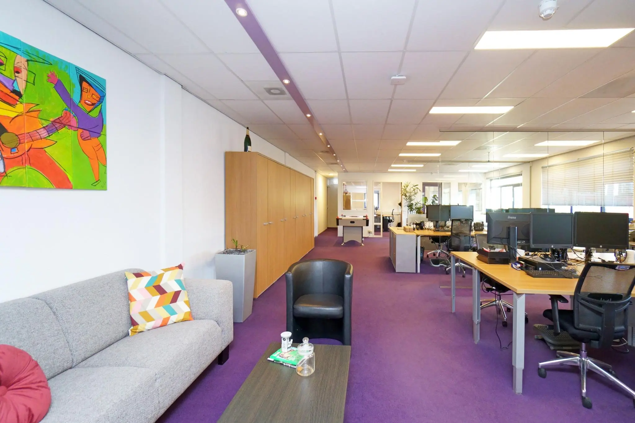Modern kantoorinterieur aan de Zuiderweg met paarse vloerbedekking, bureaus met computers, een zithoek en kleurrijke wanddecoratie.