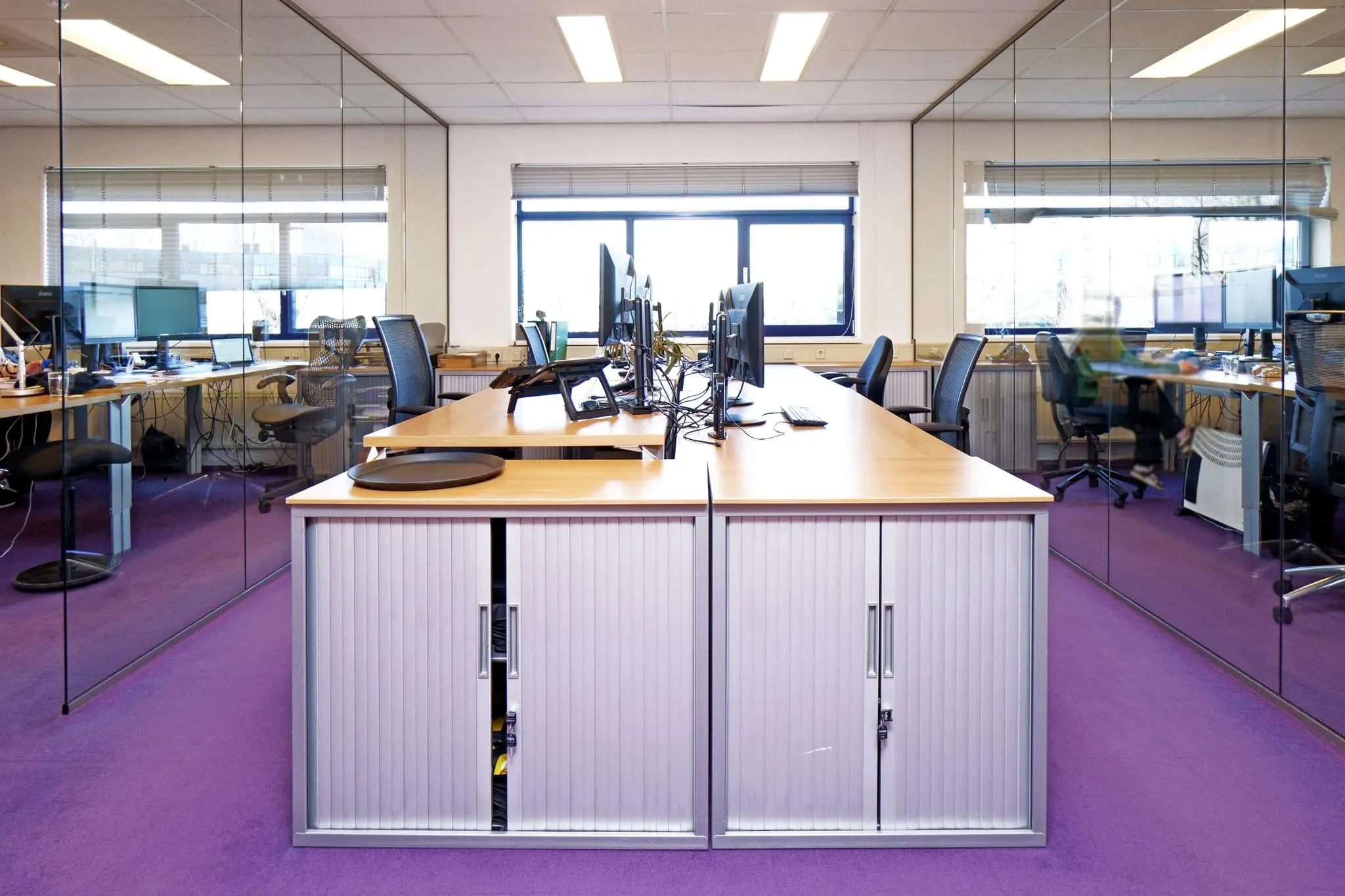 Modern kantoor met glazen wanden, paarse vloerbedekking en werkplekken met meerdere beeldschermen aan de Zuiderweg.
