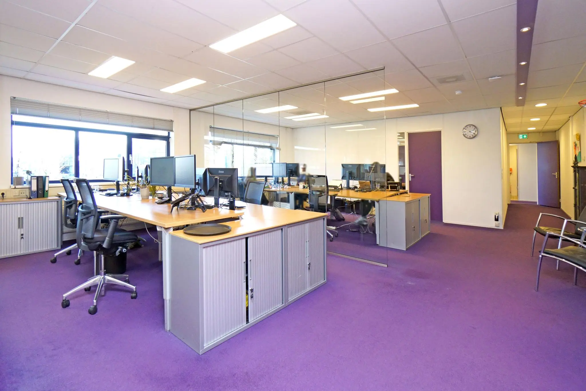 Modern kantoorinterieur aan de Zuiderweg met paarse vloerbedekking, werkplekken met computers en glazen vergaderwand.