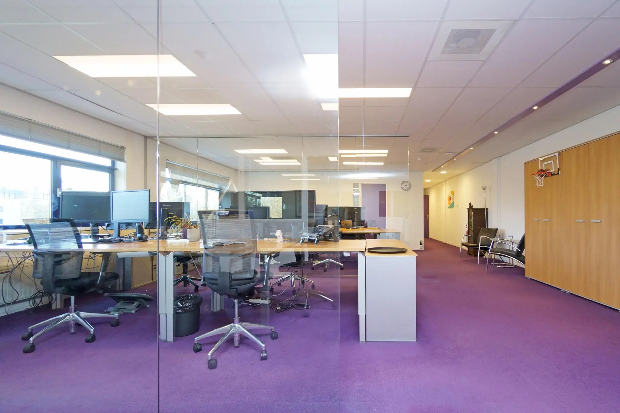 Modern kantoor met paarse vloerbedekking, glazen wanden en meerdere werkplekken met bureaustoelen en computerschermen aan de Zuiderweg.