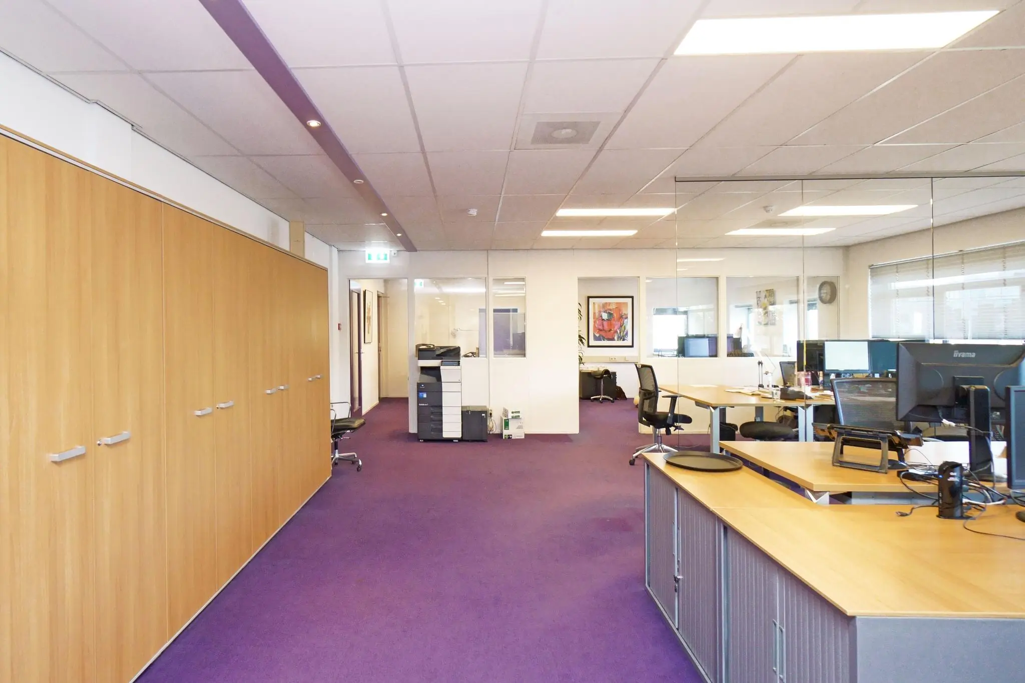 Modern kantoorinterieur aan de Zuiderweg met paarse vloerbedekking, glazen wanden en meerdere werkplekken.