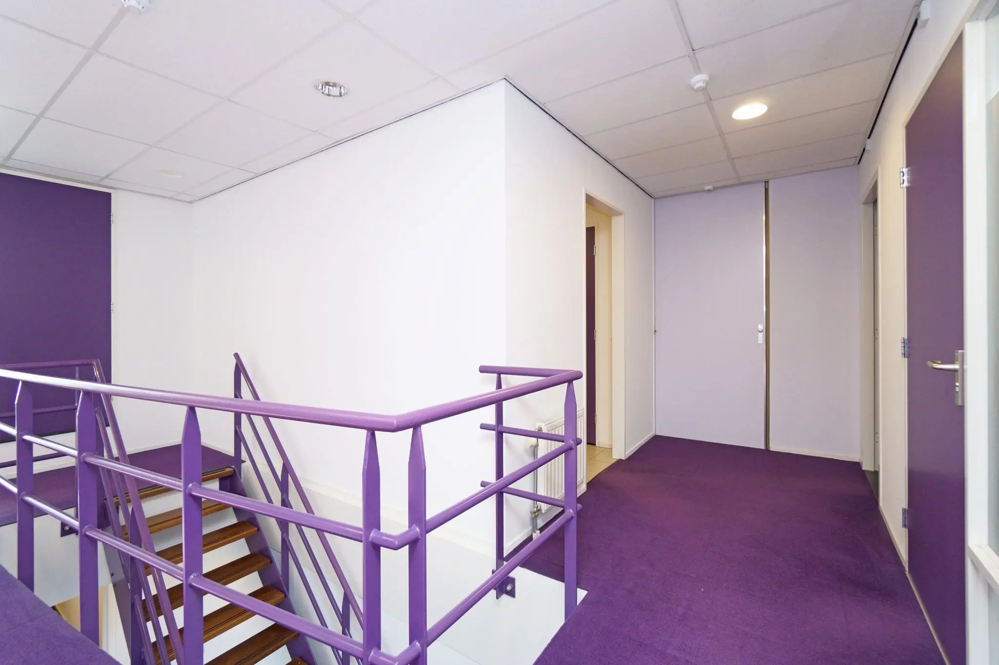 Trapopgang en overloop met paarse leuningen, deuren en vloerbedekking in een pand aan de Zuiderweg.
