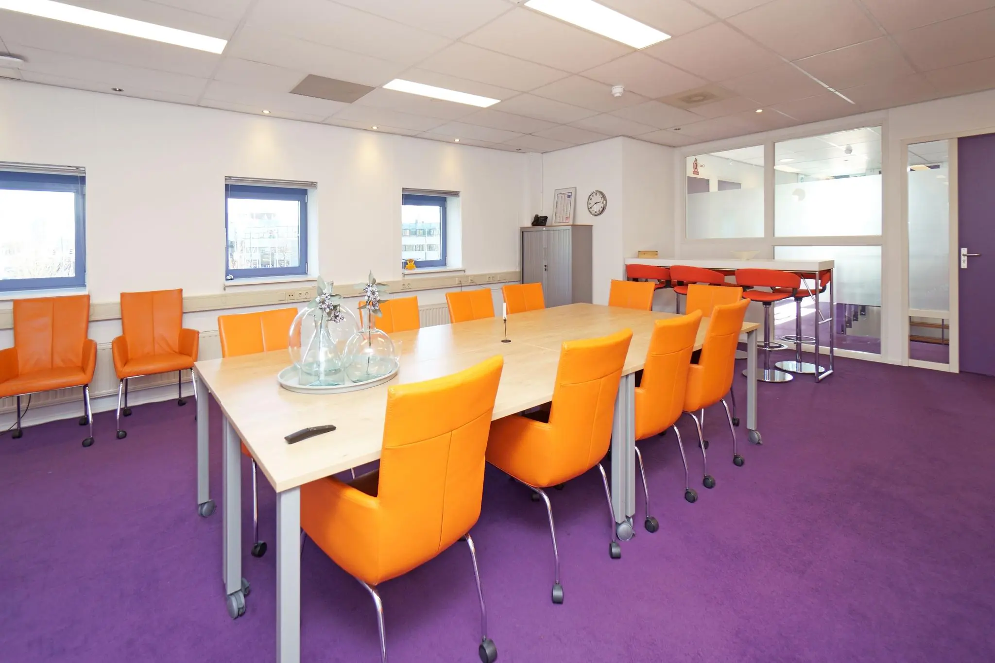 Vergaderruimte aan de Zuiderweg met paarse vloer, oranje stoelen en een grote houten tafel.