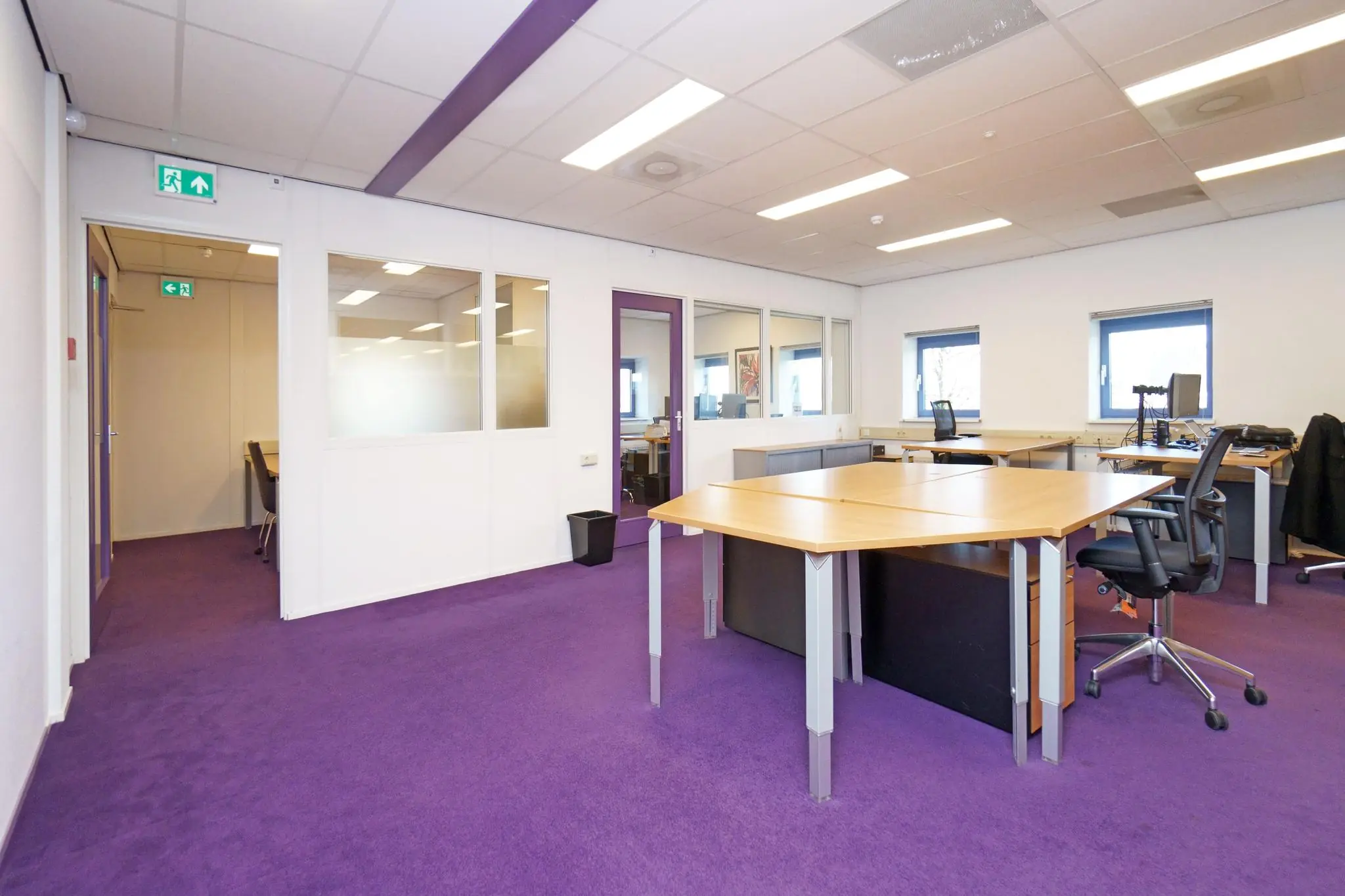 Modern kantoorinterieur aan de Zuiderweg met paarse vloerbedekking, houten bureaus en glazen binnenwanden.