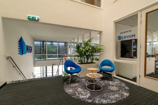 Wachtgedeelte bij MVGM-kantoor met moderne stoelen, planten en een ronde vloerkleed.