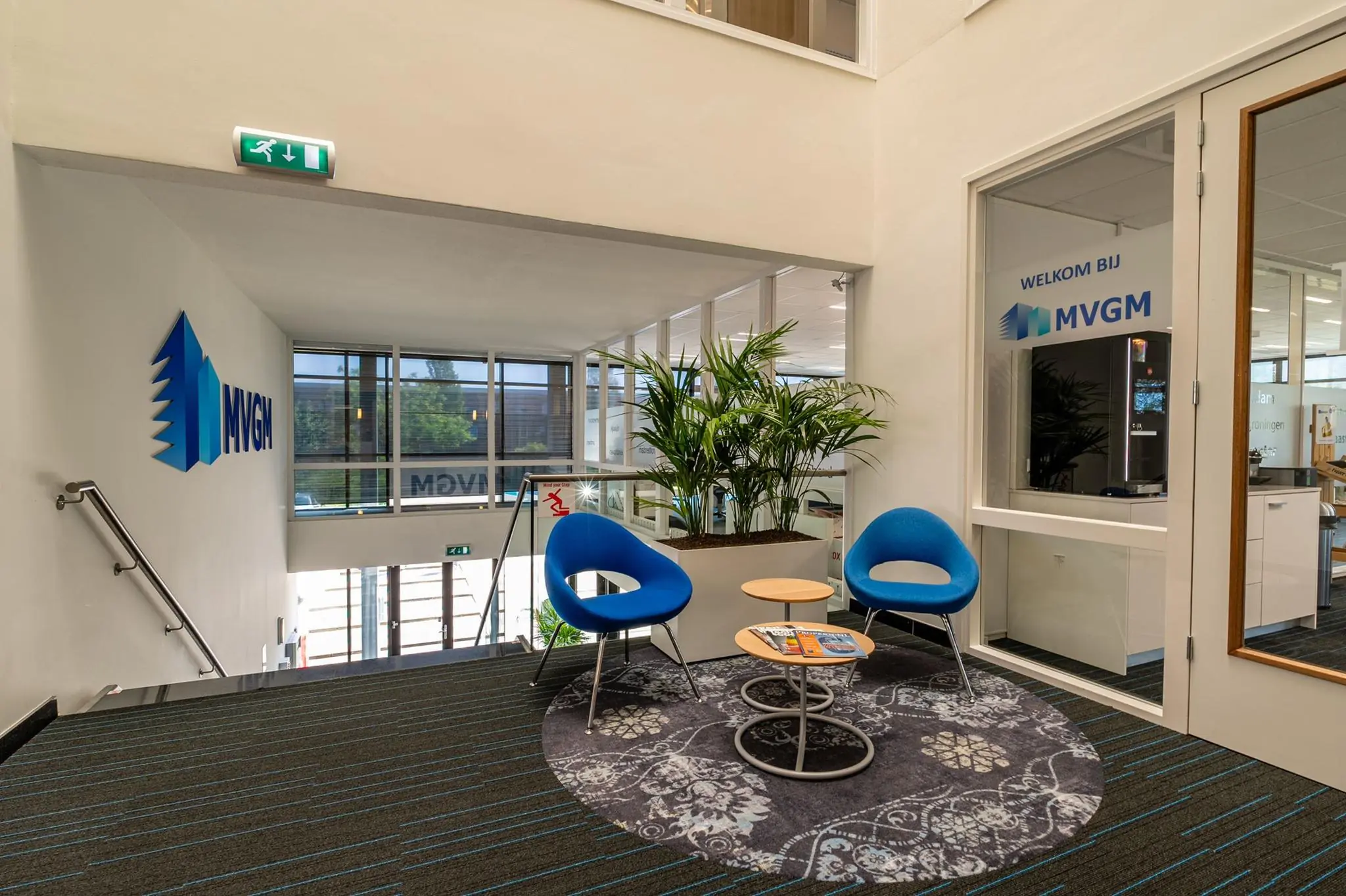 Wachtgedeelte bij MVGM-kantoor met moderne stoelen, planten en een ronde vloerkleed.