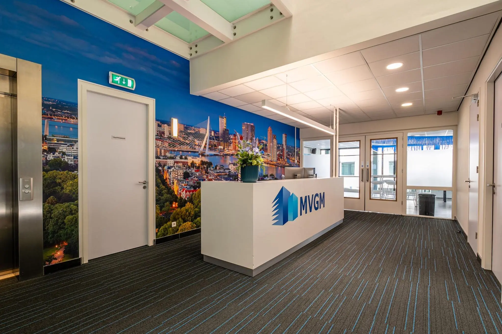 Moderne receptieruimte van MVGM aan de Bahialaan met een grote stadsfoto van Rotterdam op de wand.
