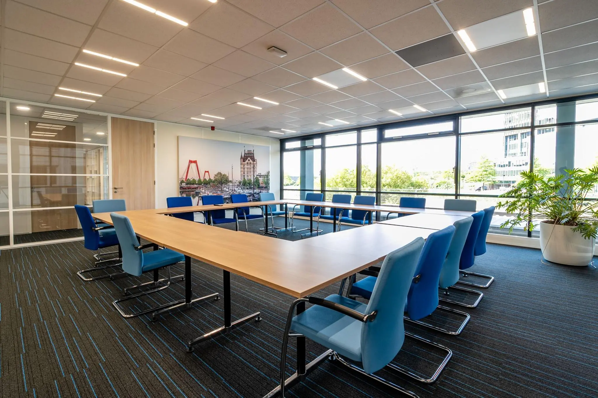 Moderne vergaderruimte aan de Bahialaan met U-vormige tafelopstelling, blauwe stoelen en grote ramen met uitzicht op groen.