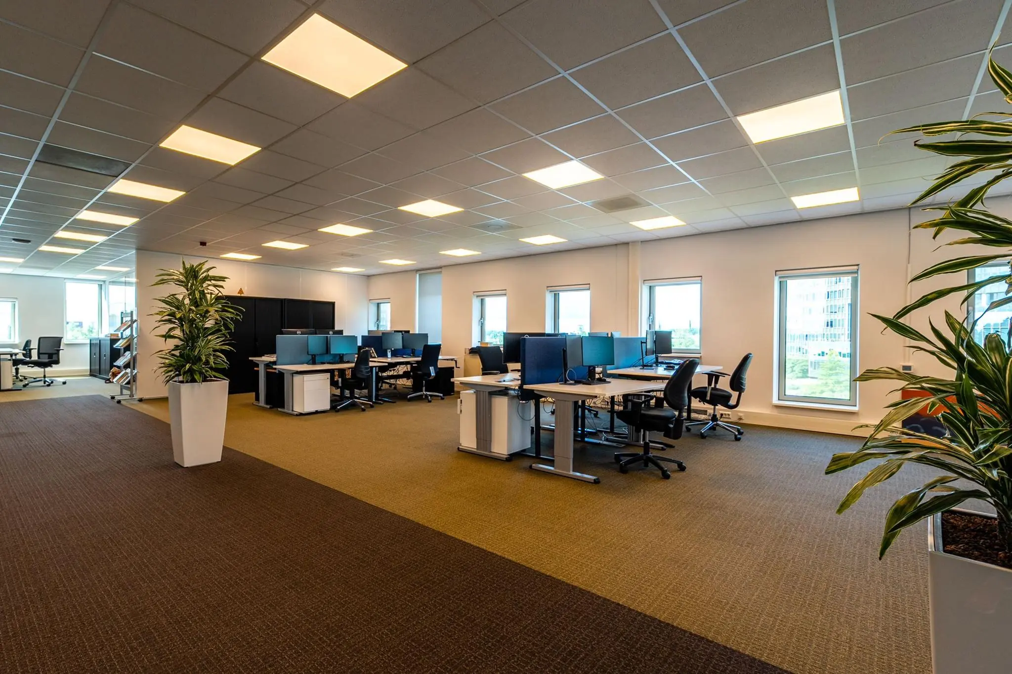 Ruim, modern kantoor met meerdere werkplekken, bureaustoelen, computers en grote ramen aan de Bahialaan.