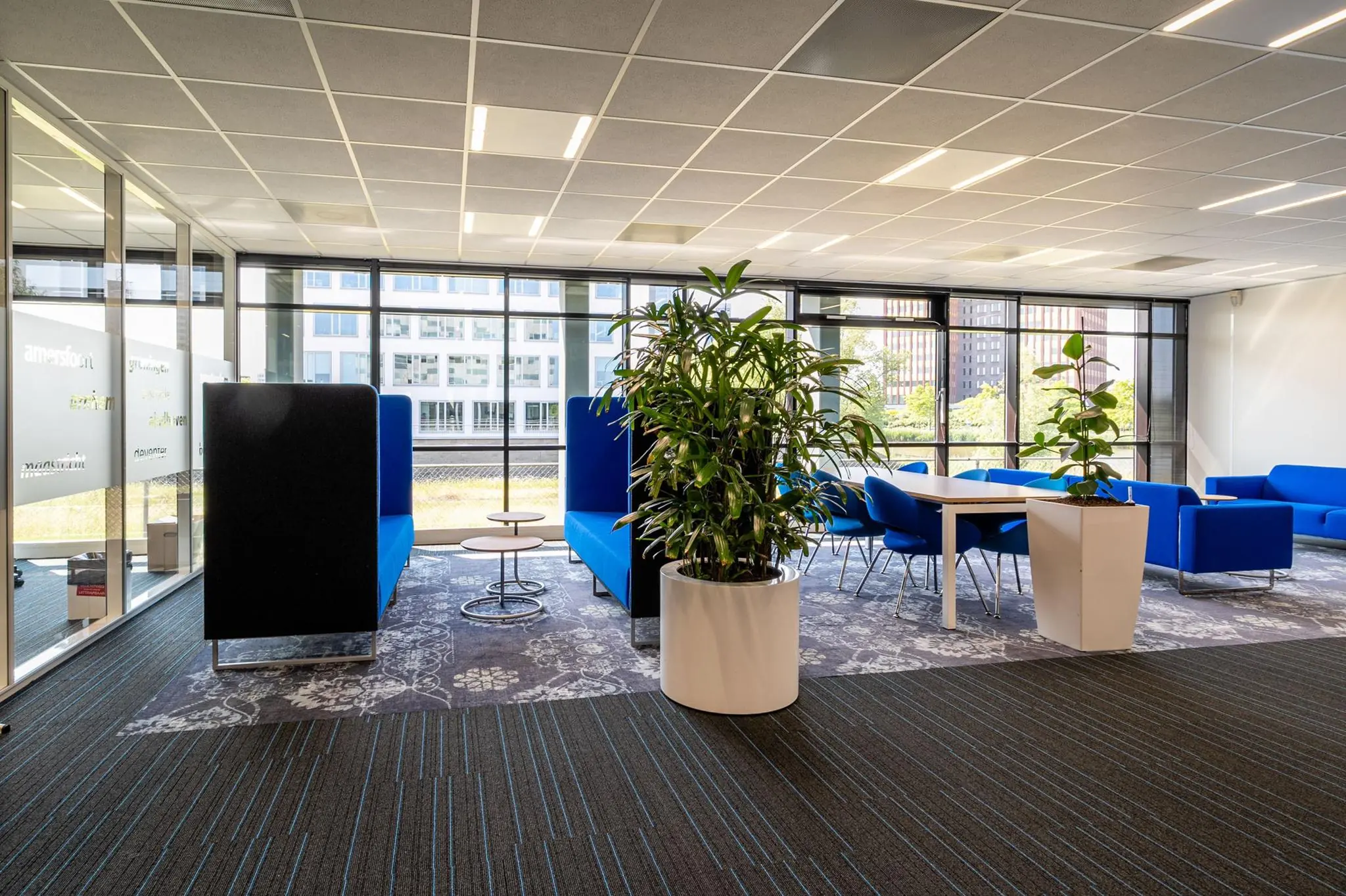 Moderne kantoorruimte aan de Bahialaan met blauwe zitmeubels, vergadertafels en grote raampartijen.