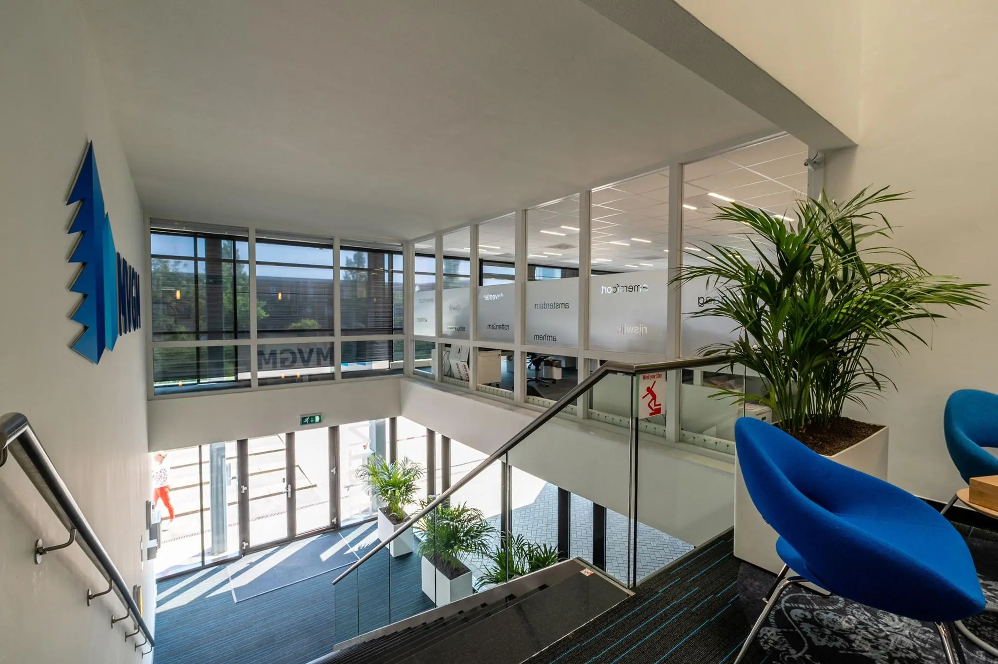 Moderne kantoorentree aan de Bahialaan met glazen wanden, blauwe stoelen en het MVGM-logo op de muur.