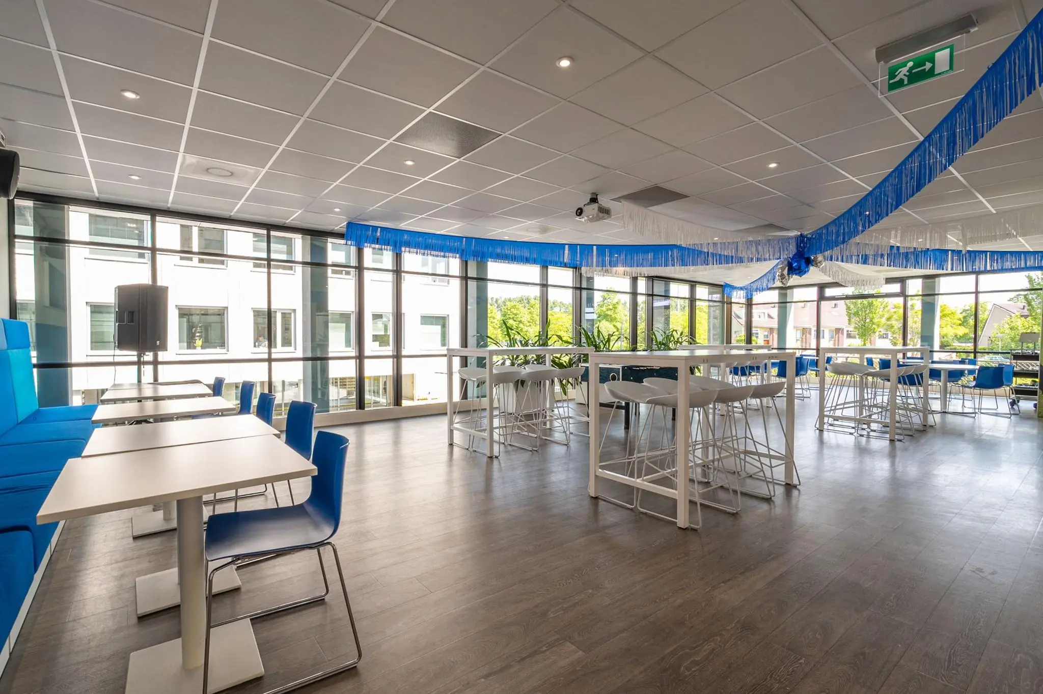 Modern ingerichte kantineruimte aan de Bahialaan met hoge ramen, blauwe accenten en feestelijke slingers.