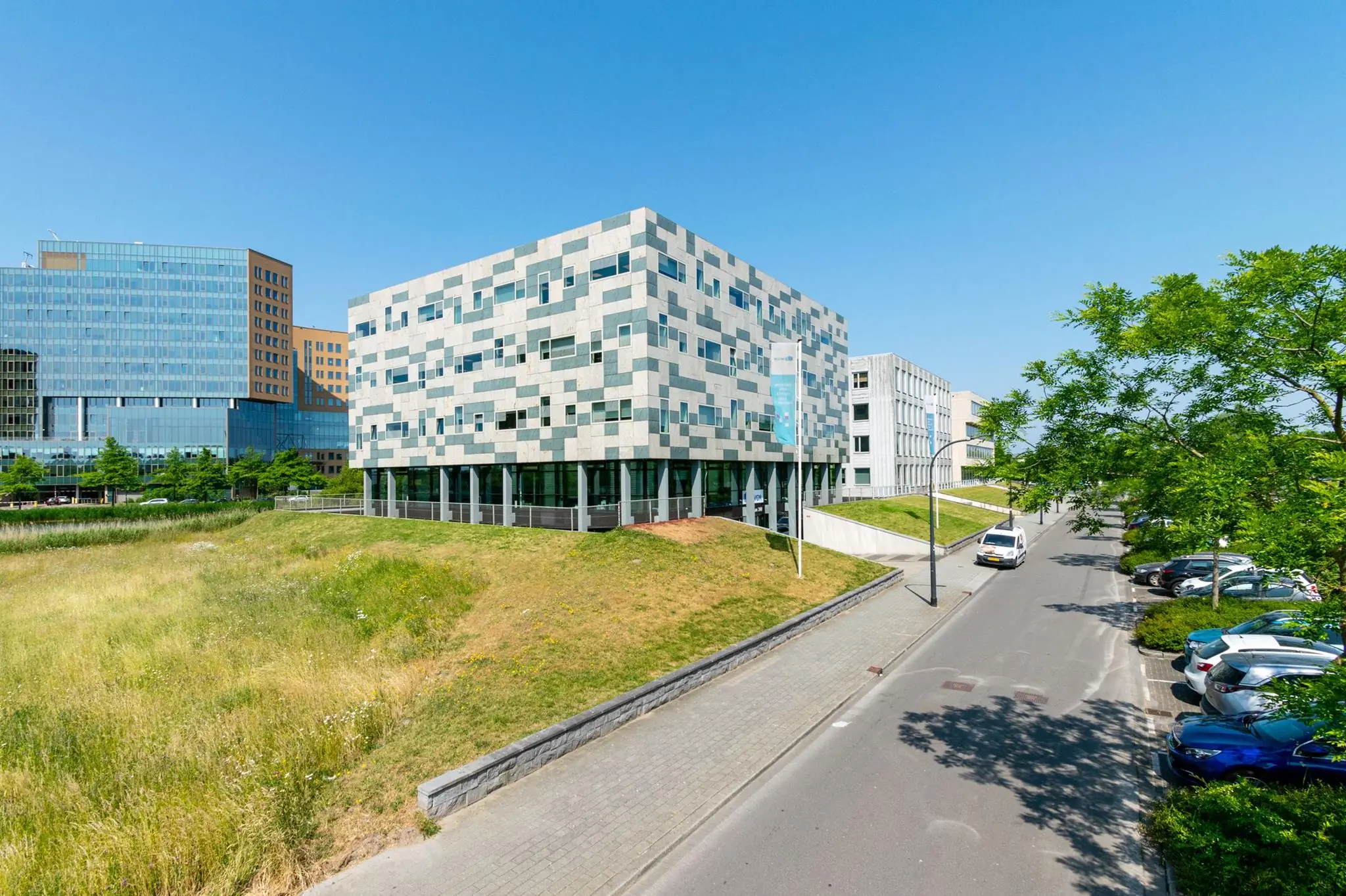 Modern kantoorgebouw aan de Bahialaan in Rotterdam met omliggend groen en parkeerplaatsen op een zonnige dag.