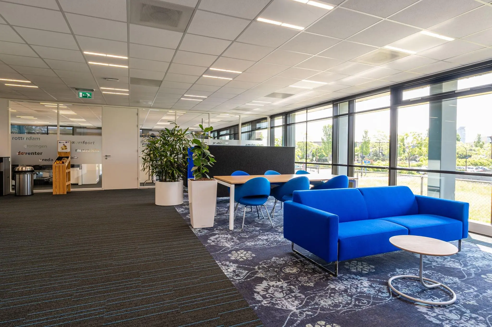 Moderne kantoorlobby aan de Bahialaan met blauwe zitbank, vergadertafel en grote ramen met uitzicht op buiten.