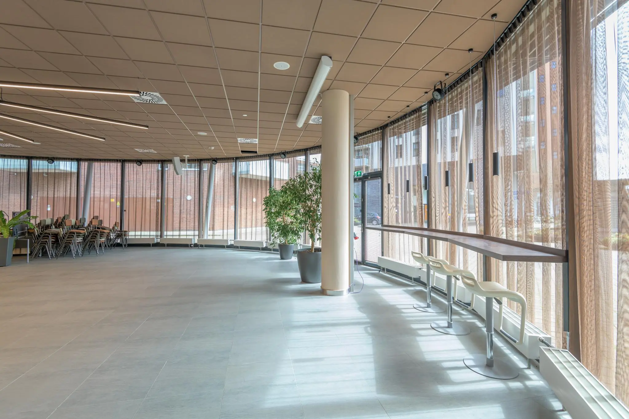 Lichte en moderne ontmoetingsruimte aan het Enthovenplein met grote raampartijen, barkrukken en gestapelde stoelen.