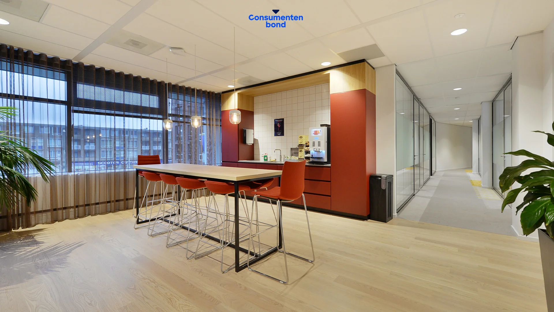 Moderne kantoorpantry met rode accenten, koffieautomaat en hoge vergadertafel op het Enthovenplein bij de Consumentenbond.