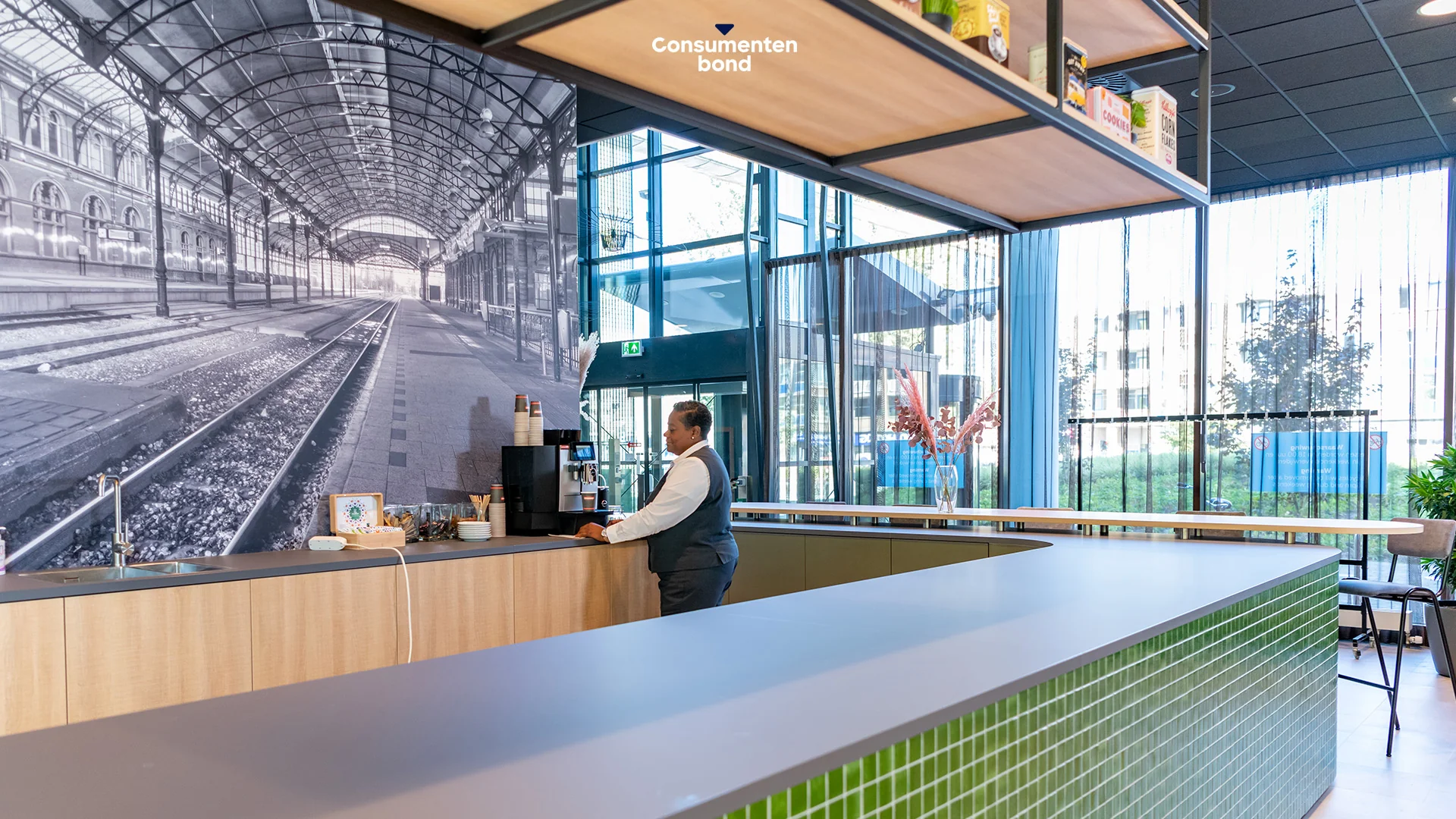 Medewerker bij koffiemachine in moderne ontvangsthal van de Consumentenbond aan het Enthovenplein.