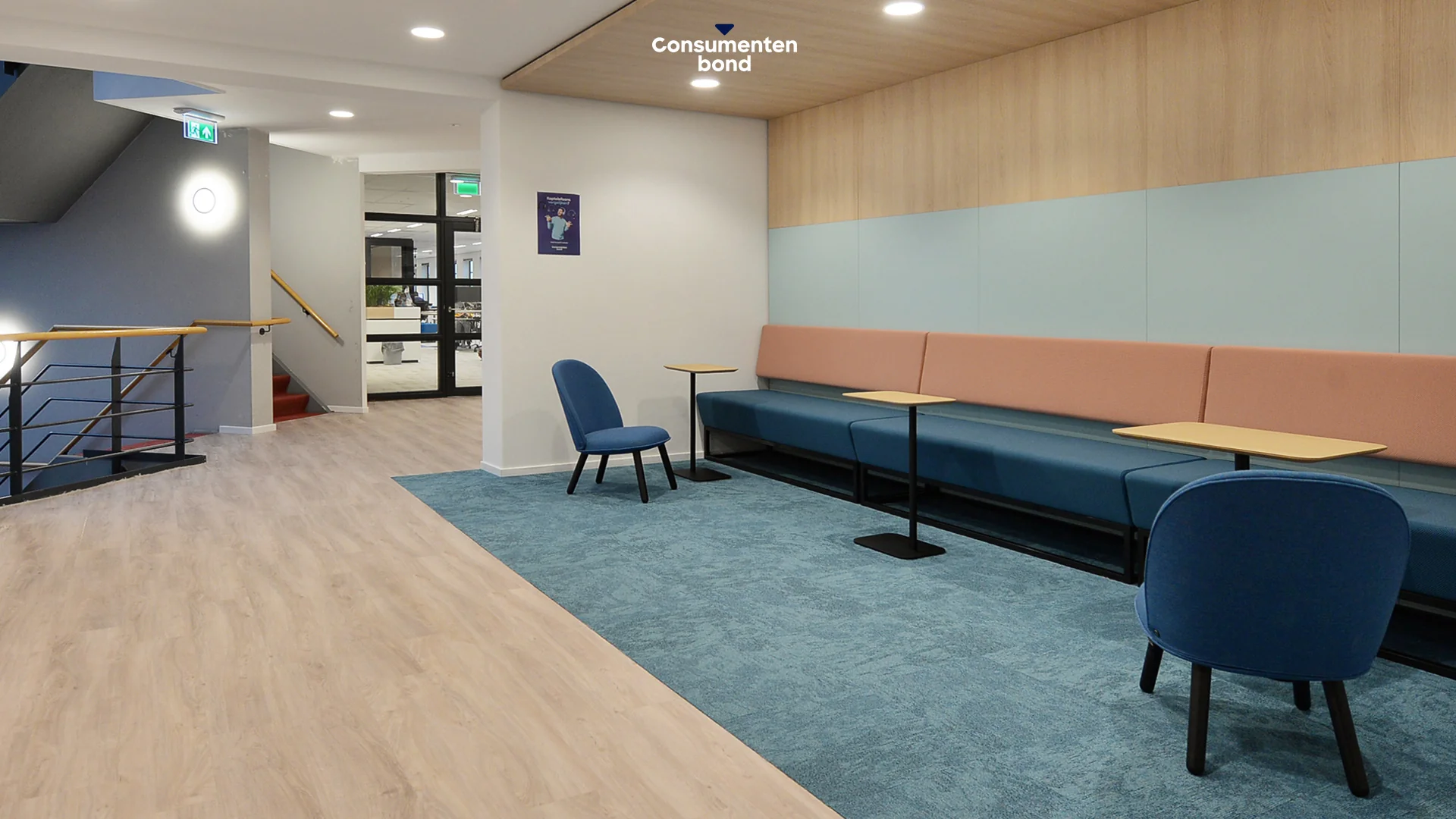 Moderne wachtruimte op het Enthovenplein binnen het kantoor van de Consumentenbond, met blauwe en roze zitplaatsen en lichte houtafwerking.