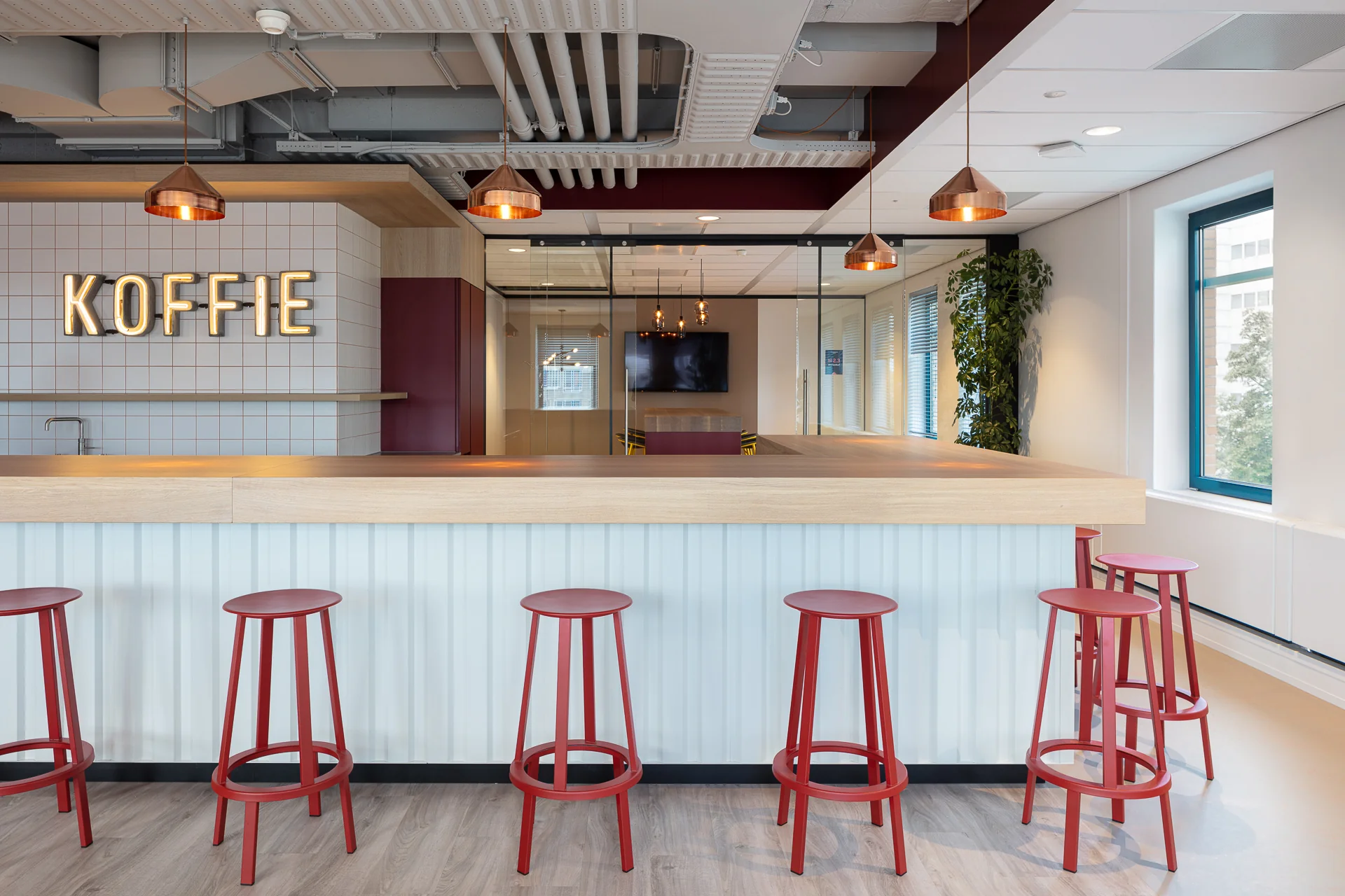 Moderne koffiehoek op het Enthovenplein met rode barkrukken, houten bar en verlichte "KOFFIE"-letters aan de muur.