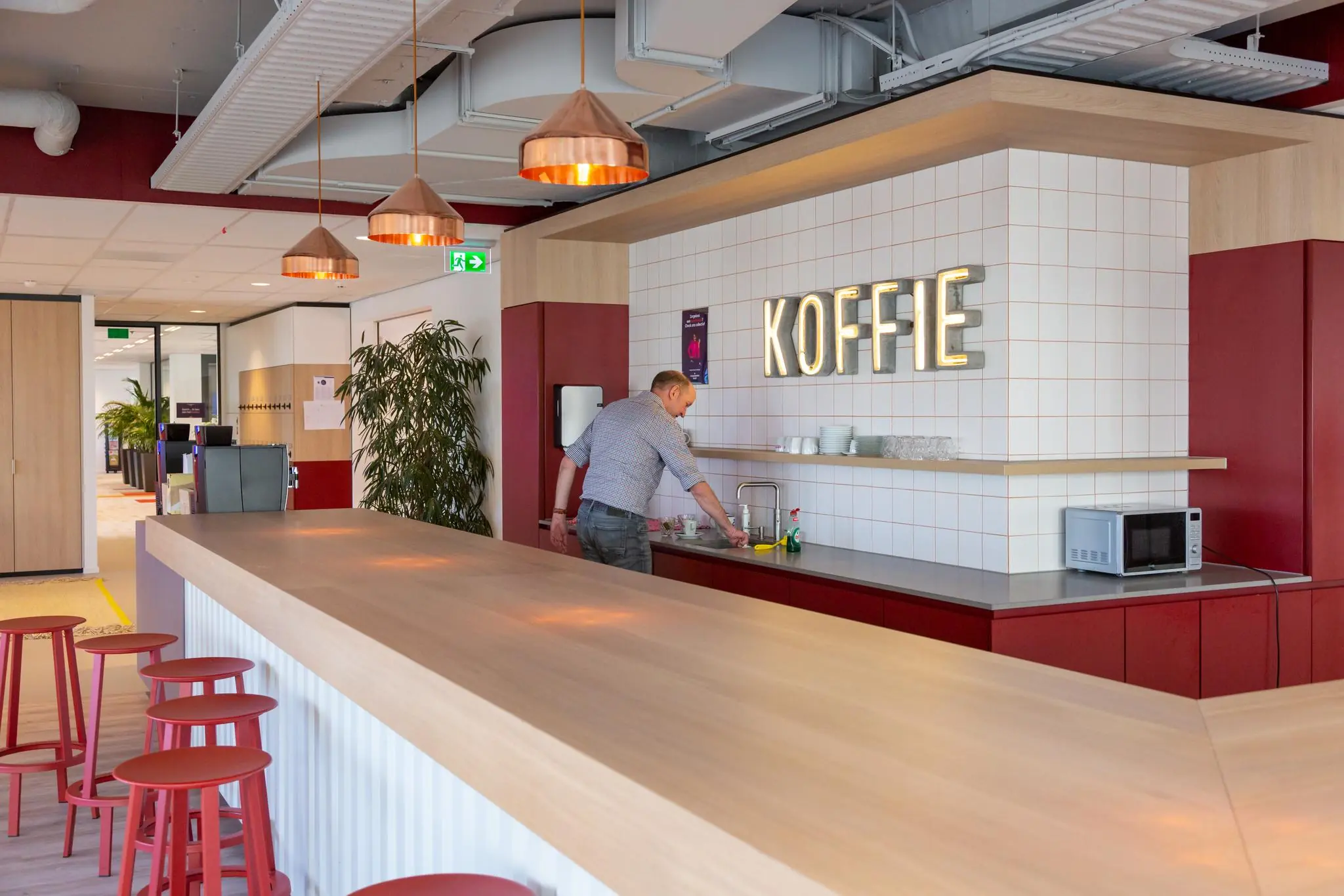 Man maakt koffie klaar in een moderne kantoorkeuken aan het Enthovenplein met een groot 'KOFFIE'-bord aan de muur.