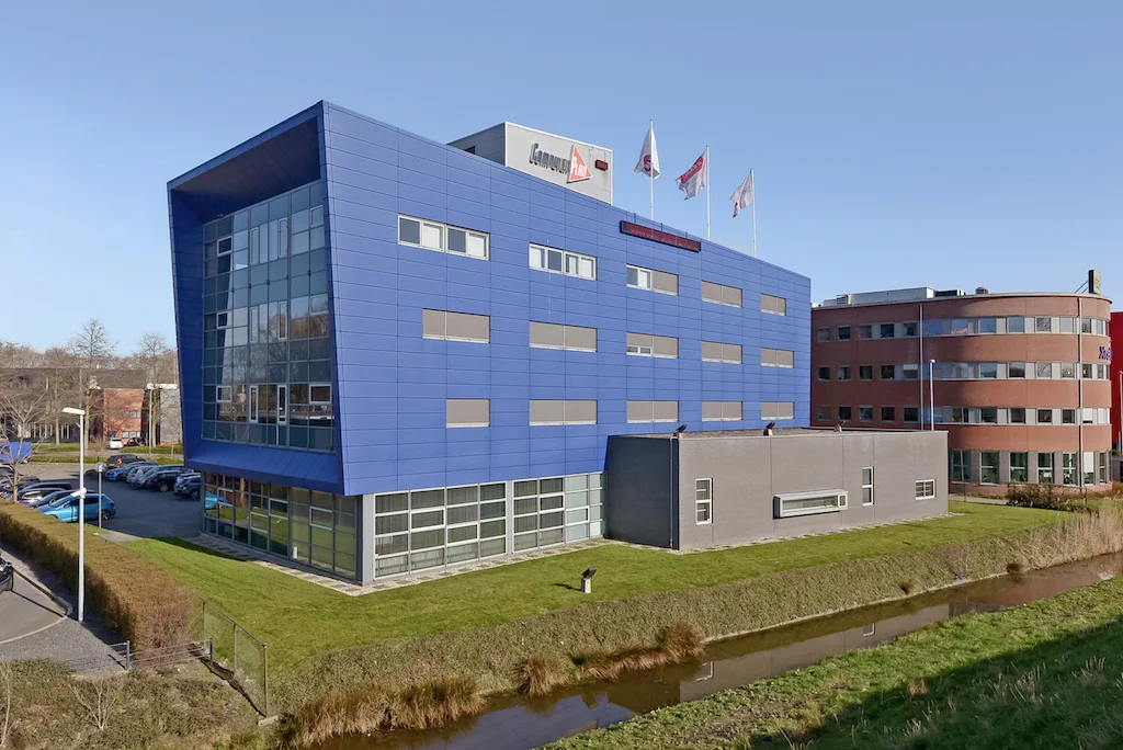 Modern kantoorgebouw aan de Kleveringweg met blauwe gevel en vlaggen op het dak, gelegen naast een waterpartij.
