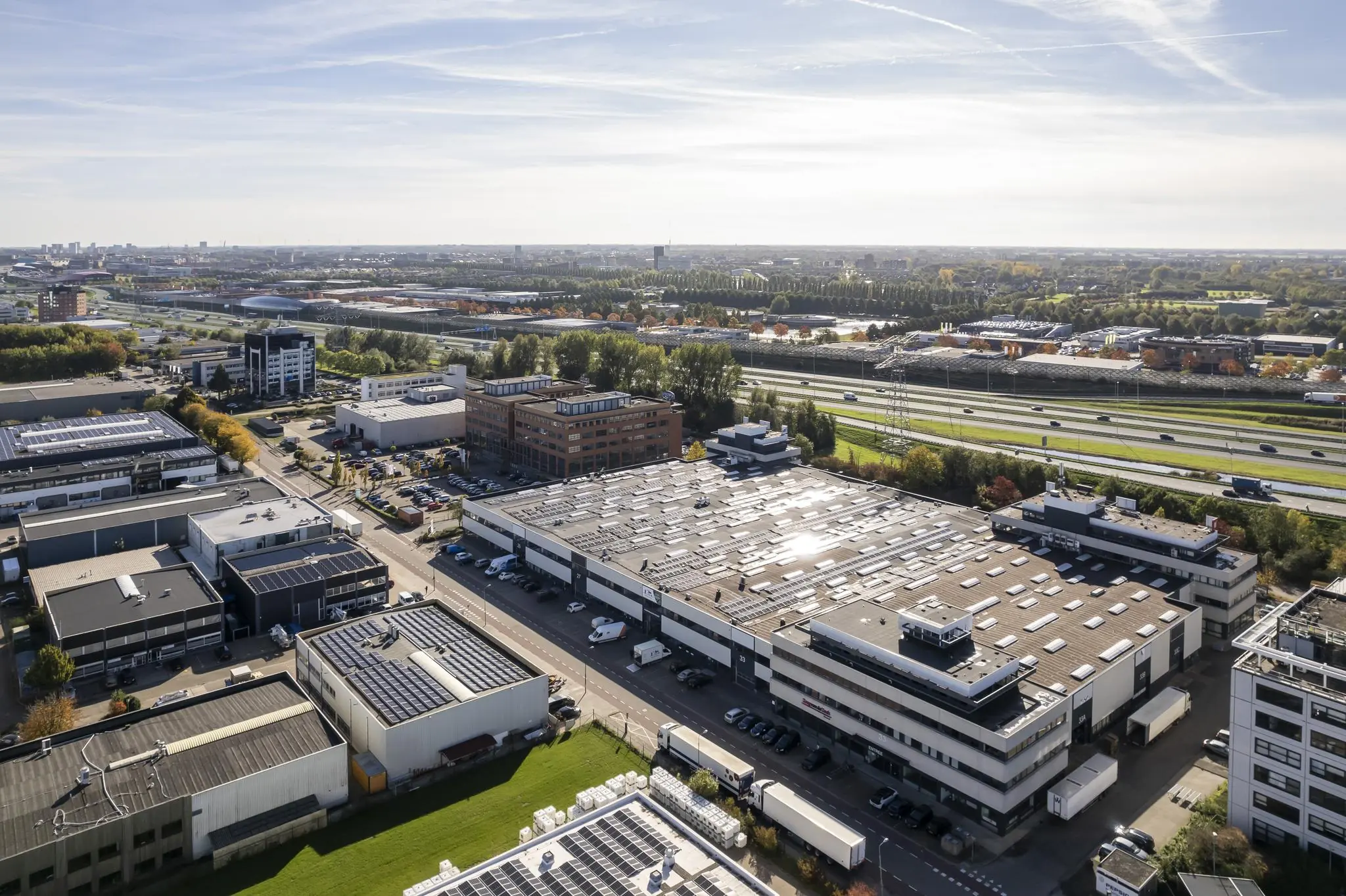 Luchtfoto van het bedrijventerrein Zonnebaan in Utrecht met magazijnen, kantoren en zonnepanelen op de daken, gelegen naast de snelweg.