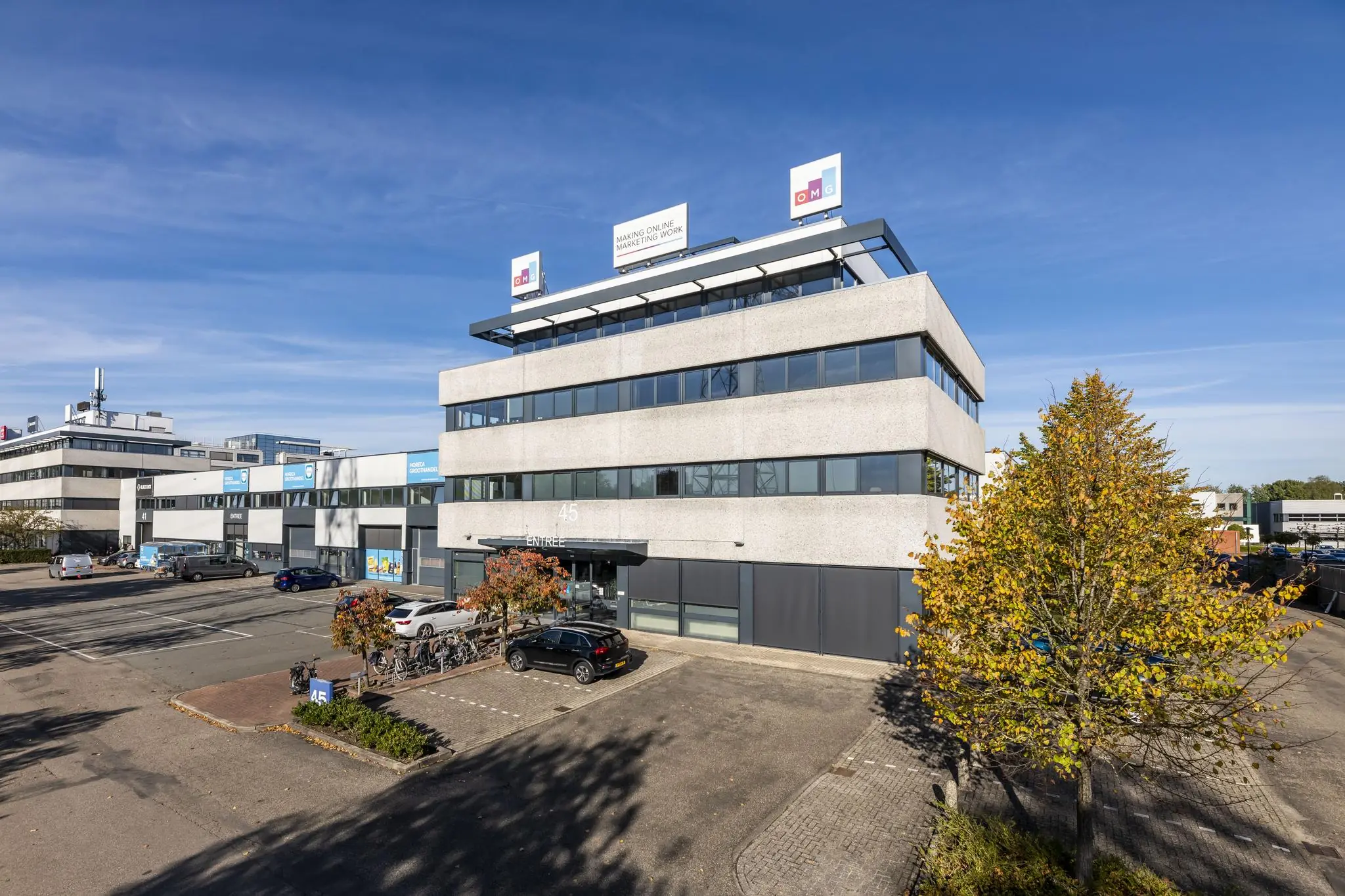 Kantoorgebouw aan de Zonnebaan 45 in Utrecht met het logo van OMG op het dak en een parkeerplaats op de voorgrond.