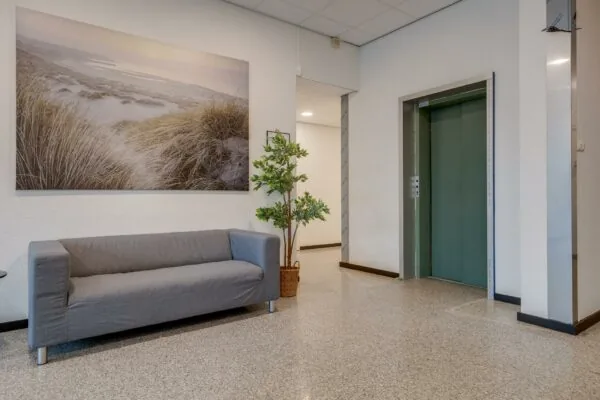 Wachtkamer of hal met grijze bank, plant, grote natuurfoto aan de muur en een groene liftdeur in gebouw aan de Zonnebaan.
