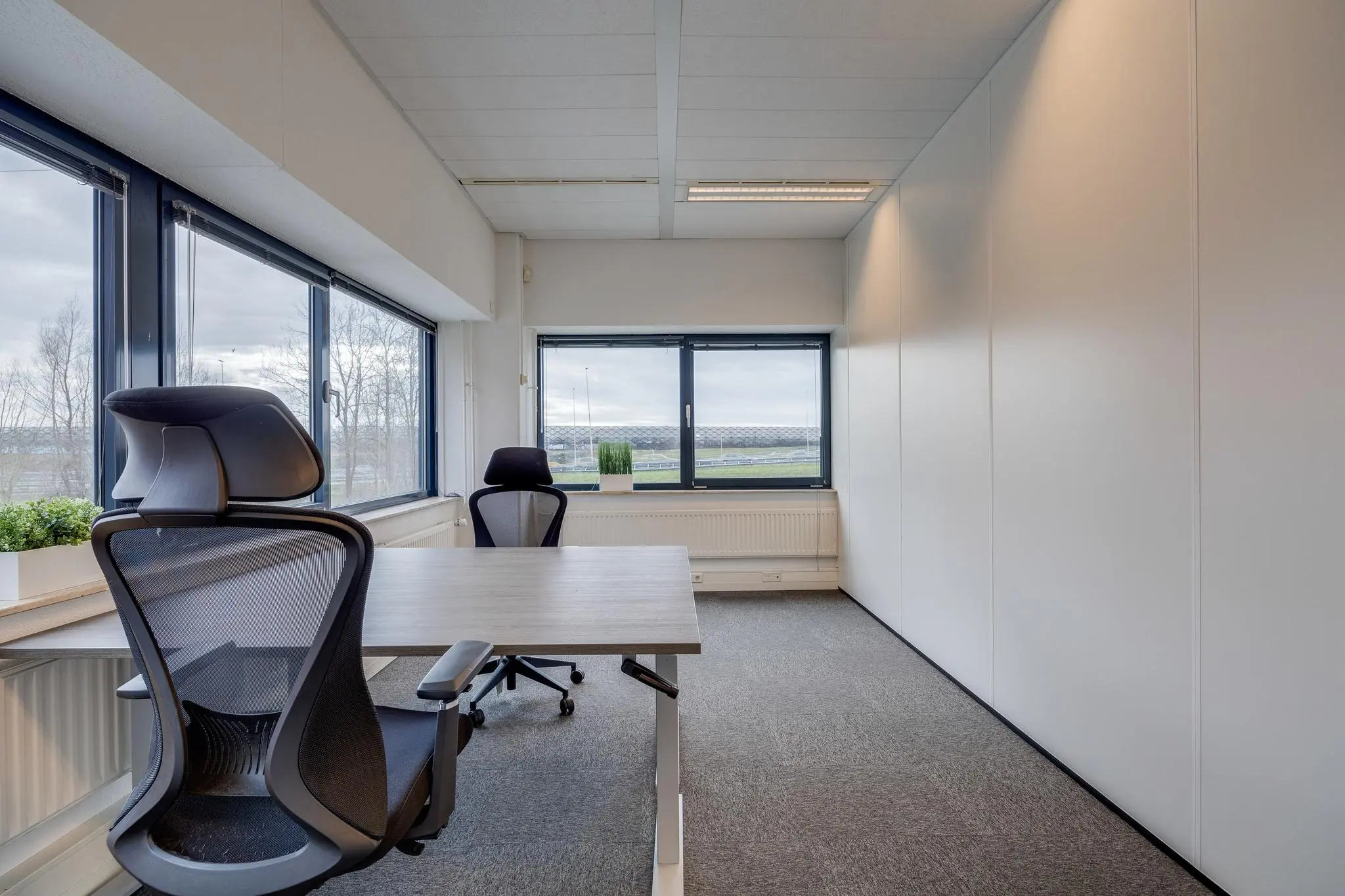 Modern, licht kantoor met twee bureaustoelen, een houten bureau en uitzicht op bedrijventerrein Zonnebaan.
