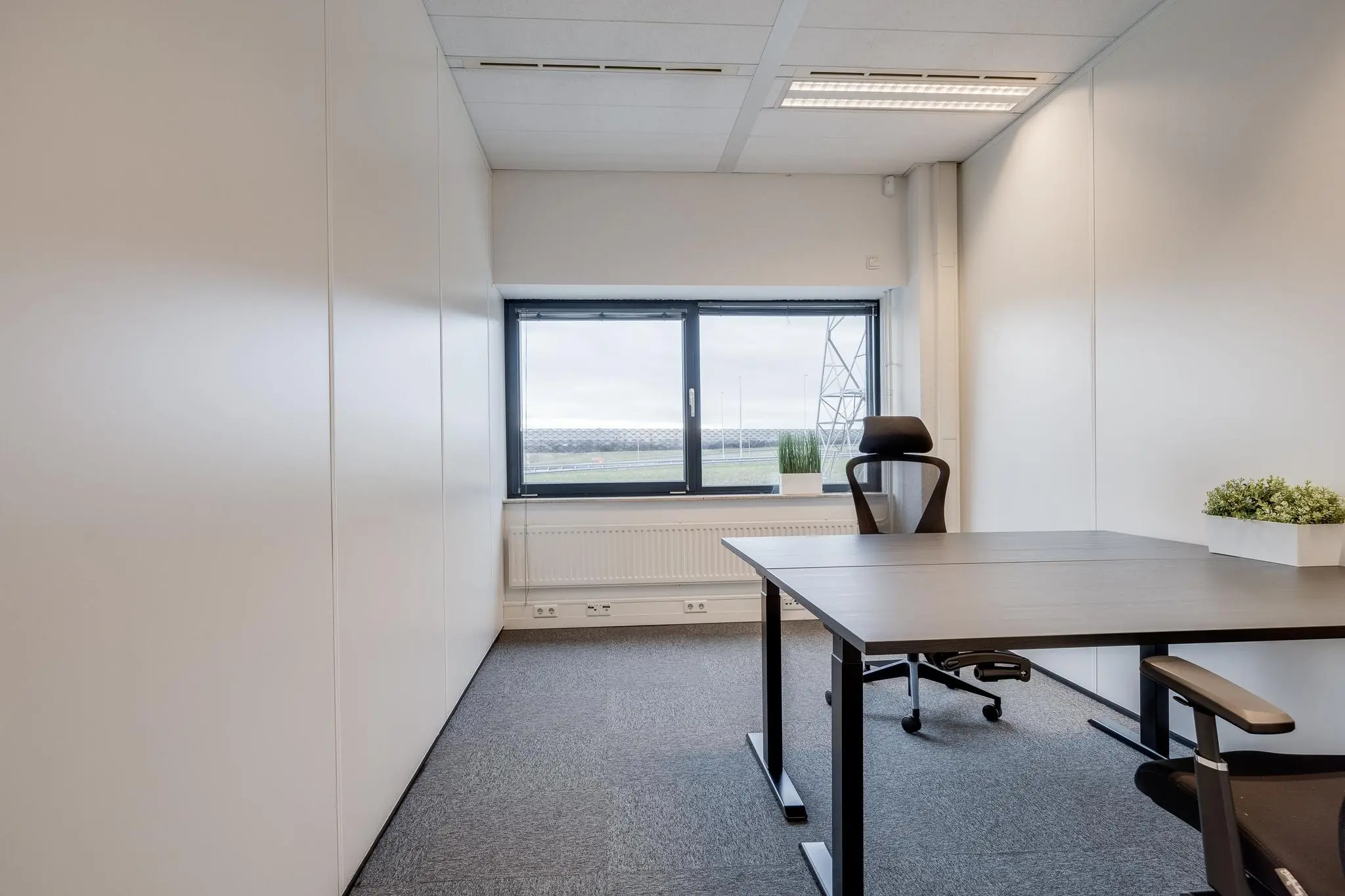 Modern, licht kantoor aan de Zonnebaan met twee bureaus, bureaustoelen en uitzicht op een open veld.