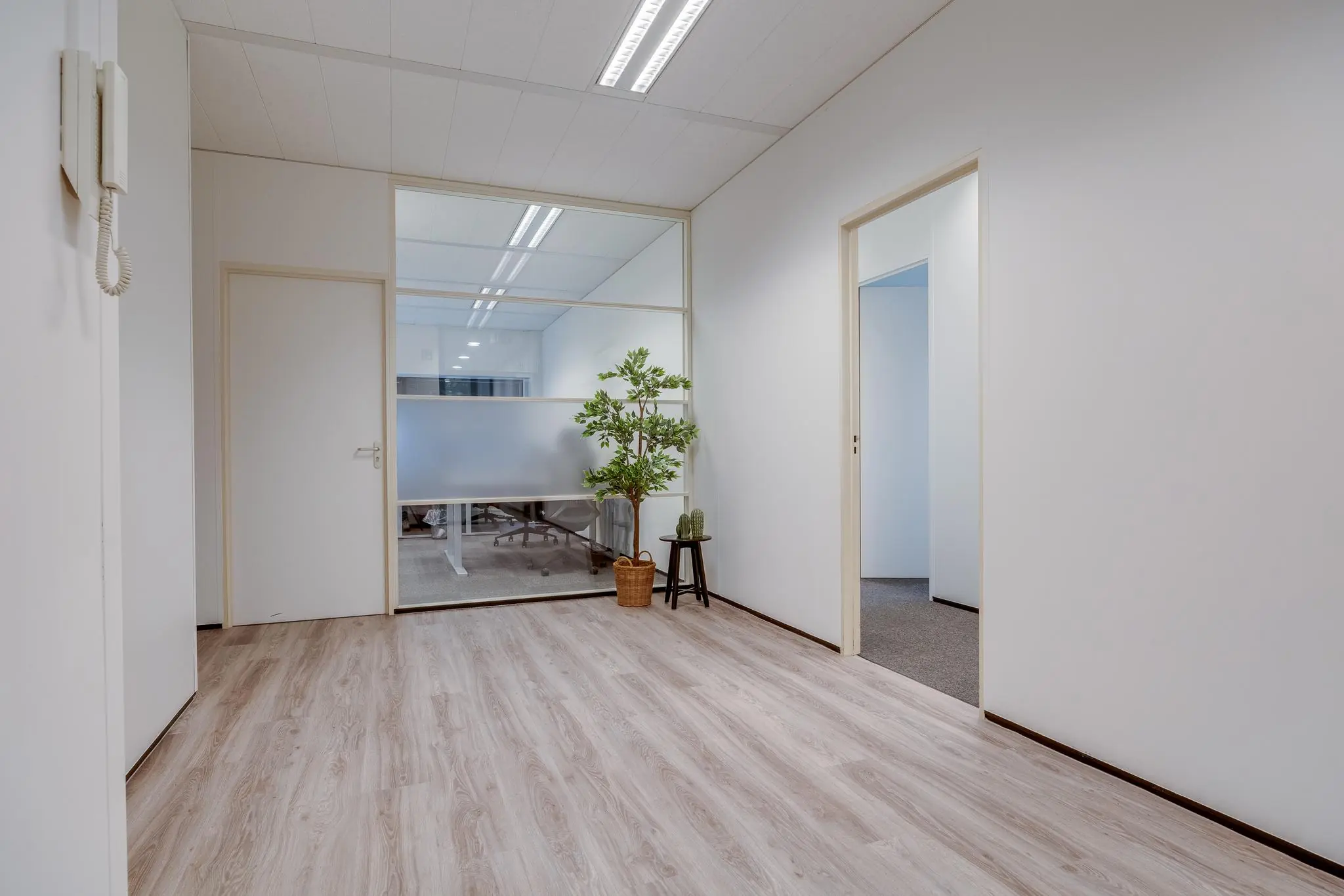Lichte kantoorruimte met houten vloer, witte muren en zicht op een vergaderruimte achter een glazen wand.