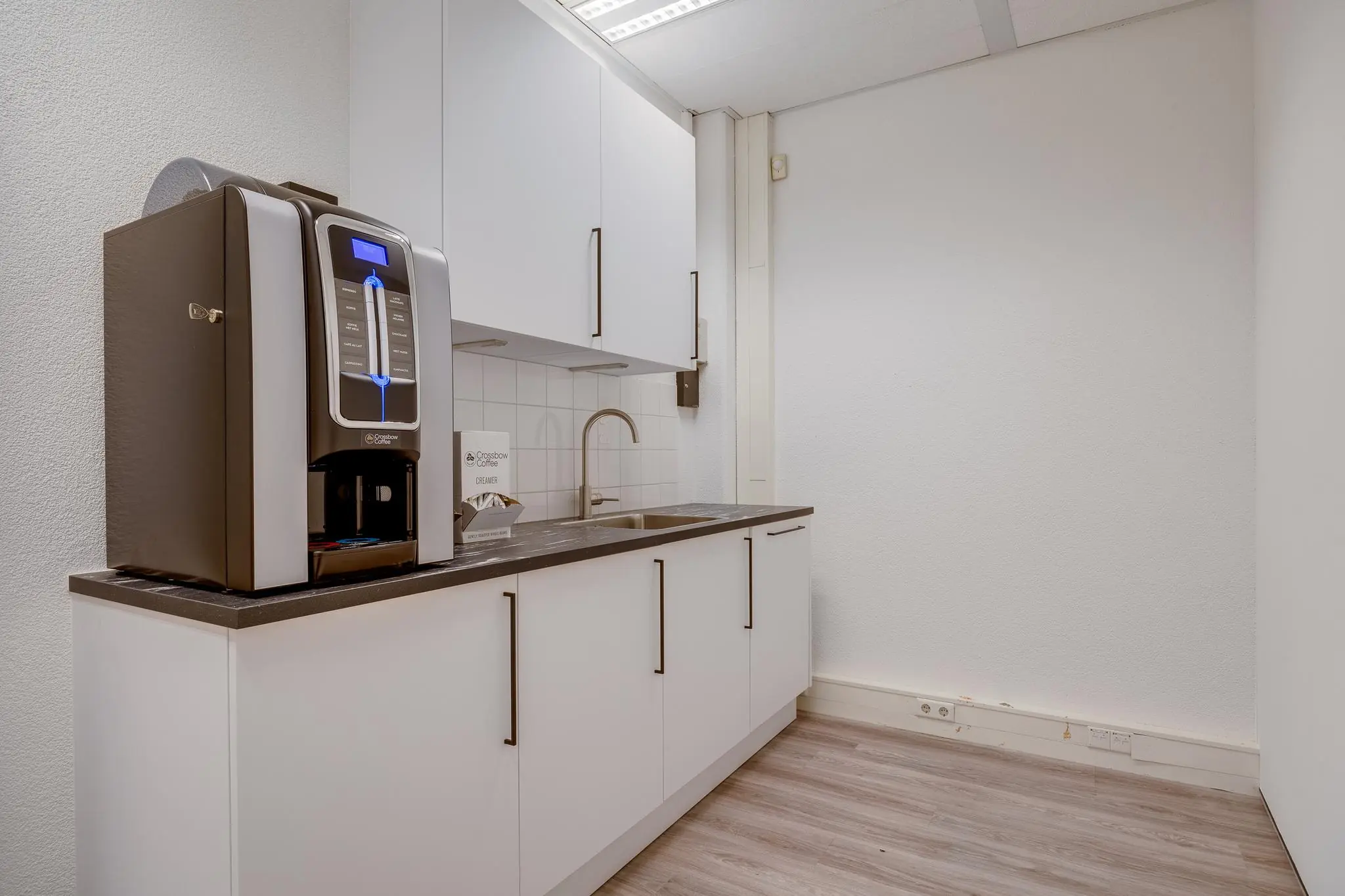Kleine pantry met witte kasten, een aanrechtblad met spoelbak en een Crossbow koffiemachine.