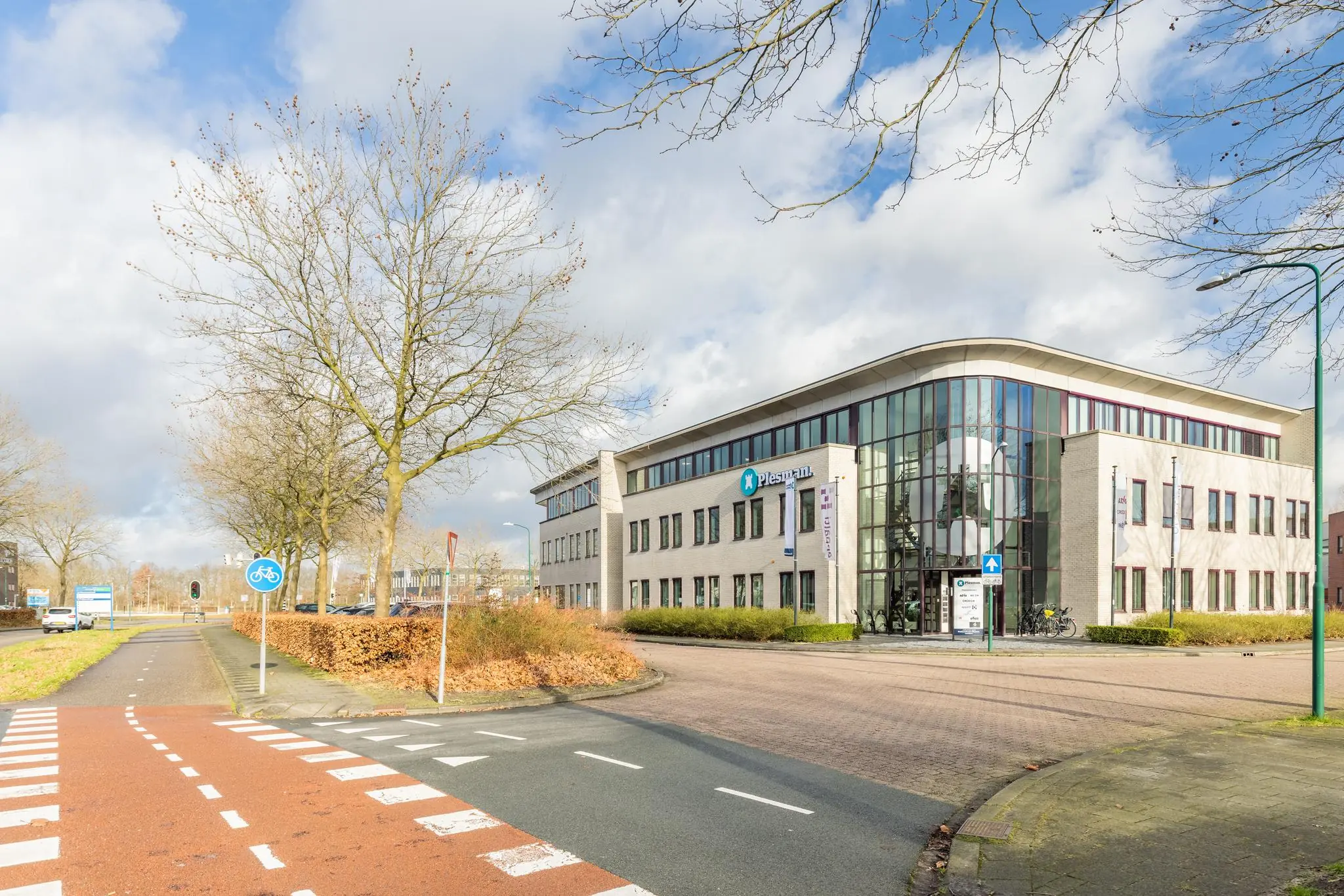 Modern kantoorgebouw aan de Plesmanstraat met glasgevel en omliggende bomen in een stedelijke omgeving.