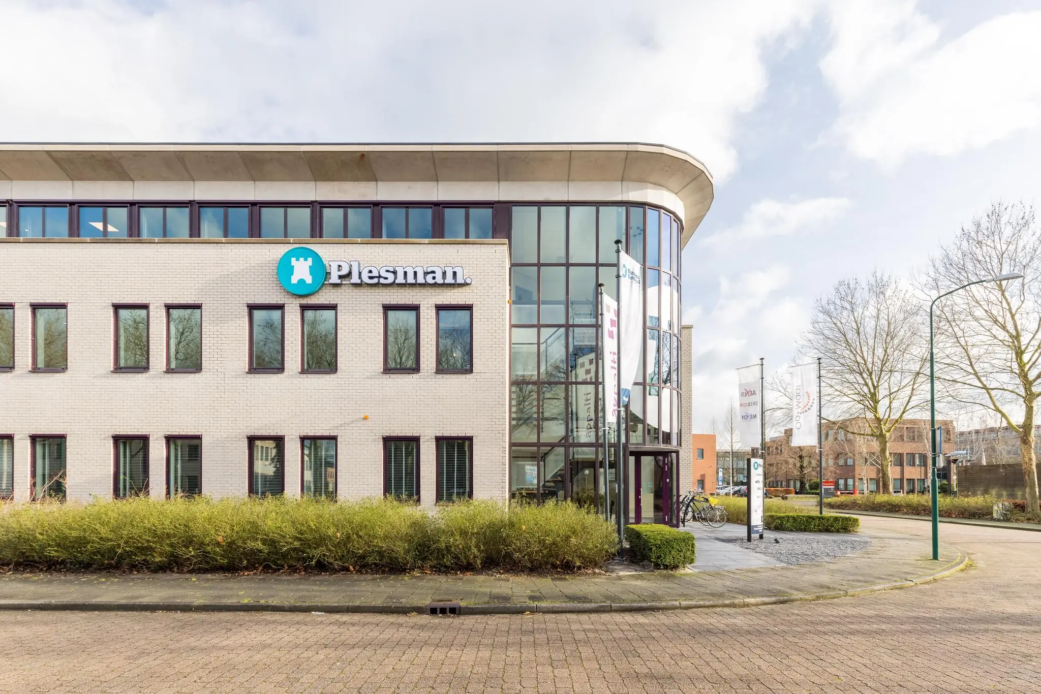 Modern kantoorgebouw aan de Plesmanstraat met het logo van Plesman op de gevel en fietsen geparkeerd bij de ingang.