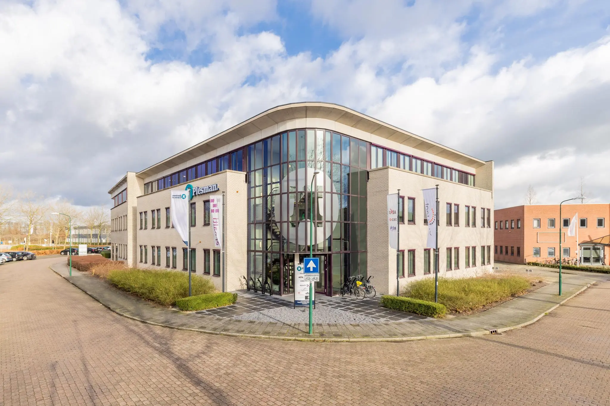 Modern kantoorgebouw aan de Plesmanstraat met glazen entree en vlaggenmast.