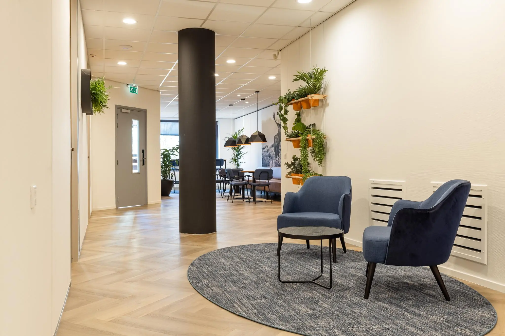 Moderne wachtruimte aan de Plesmanstraat met blauwe fauteuils, plantenwand en houten visgraatvloer.