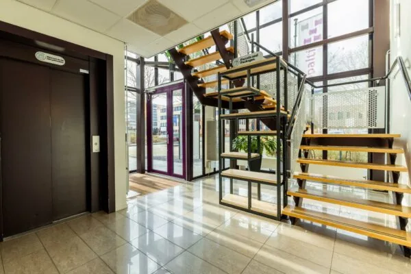 Ingangshal van een modern kantoorgebouw aan de Plesmanstraat met een houten trap, lift en glazen entree.