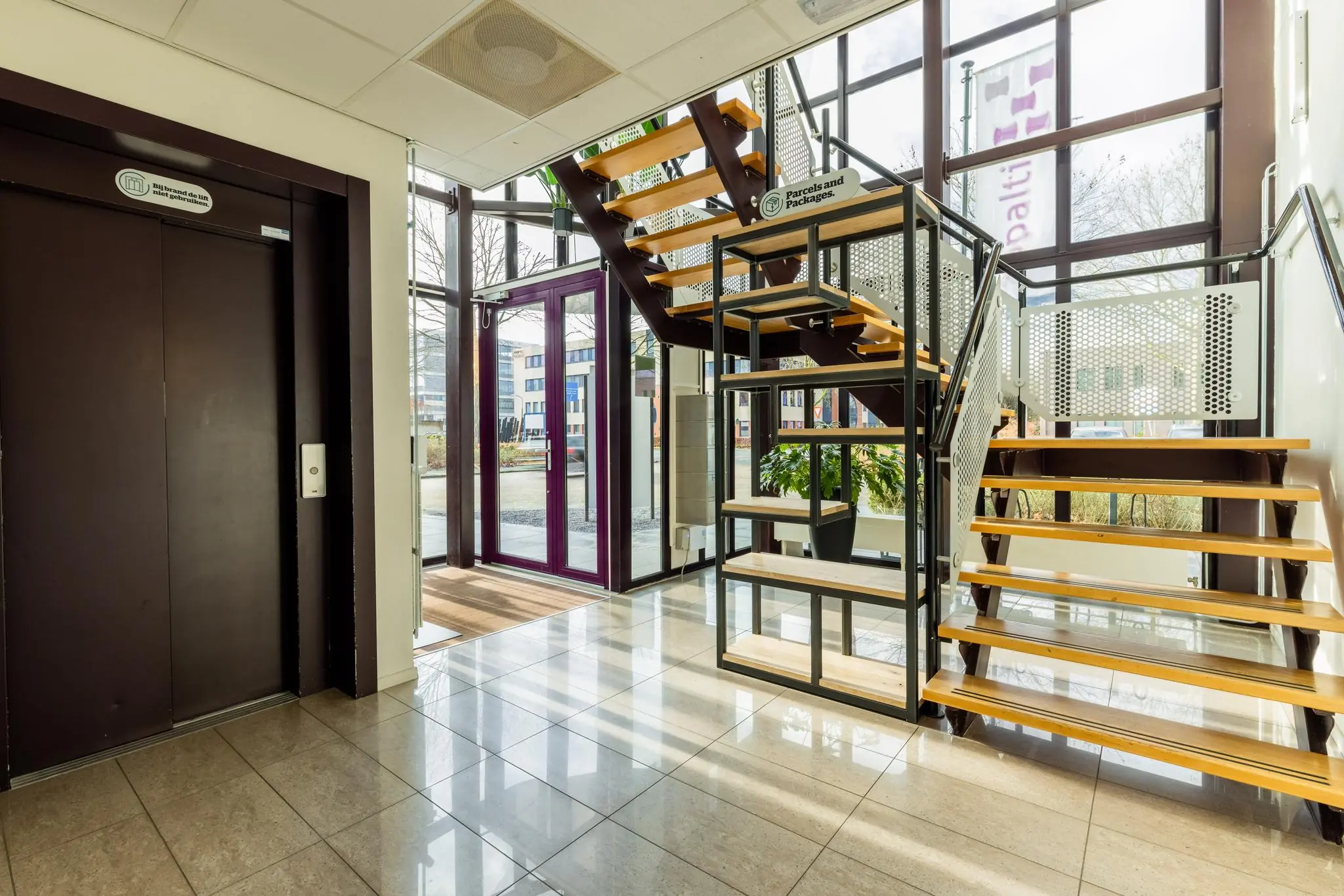 Ingangshal van een modern kantoorgebouw aan de Plesmanstraat met een houten trap, lift en glazen entree.