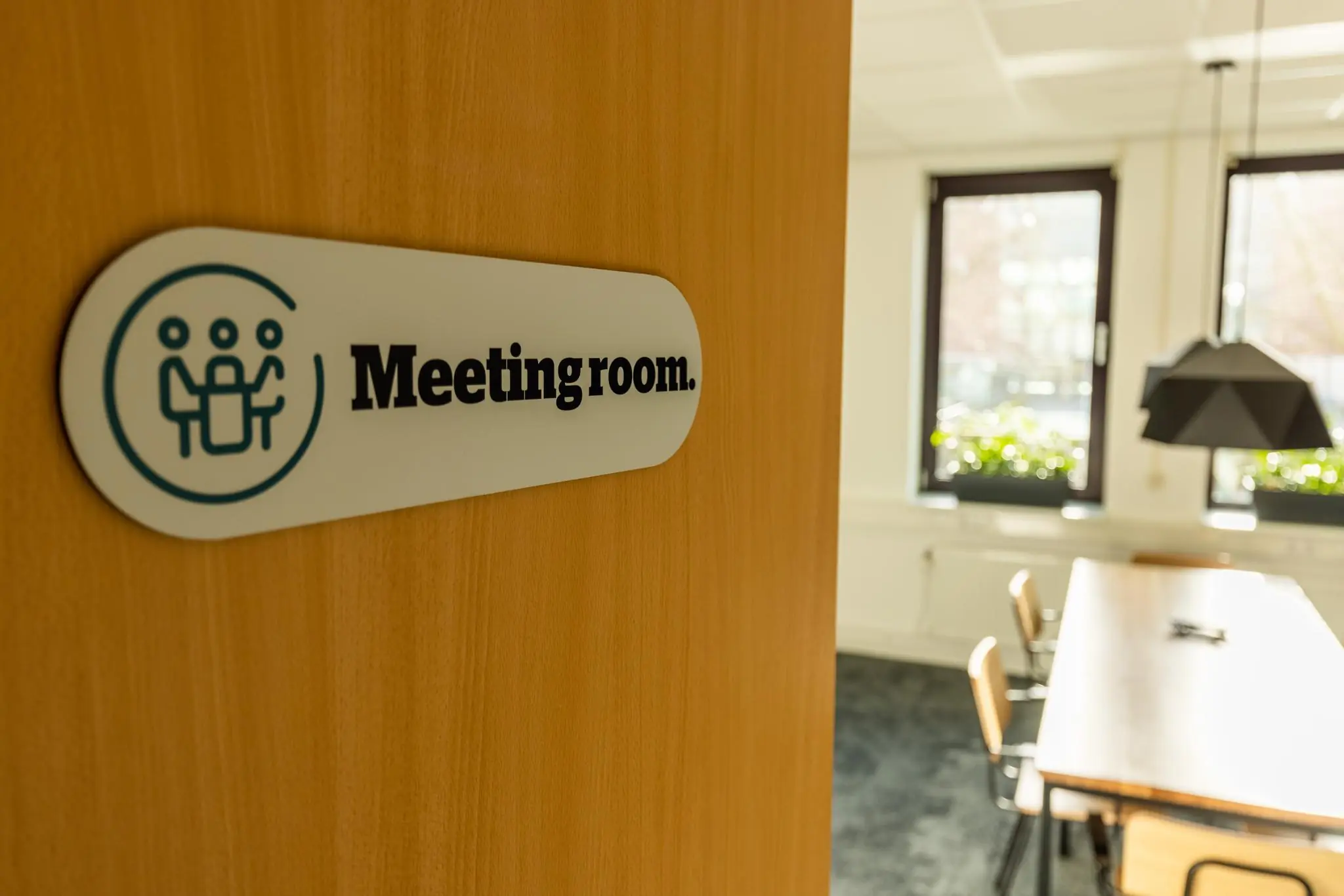 Deur met bordje "Meetingroom" opent naar een lichte vergaderruimte aan de Plesmanstraat.