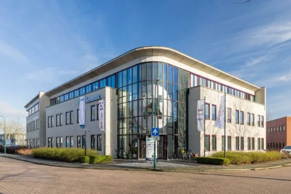 Modern kantoorgebouw aan de Plesmanstraat met glazen gevel, vlaggen en fietsenrekken bij de ingang.