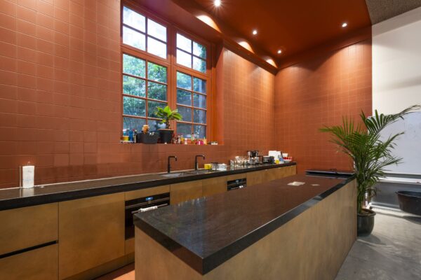 Moderne keuken met donker aanrechtblad, grote ramen en terracottakleurige wandtegels in een ruimte aan de Overtoom.