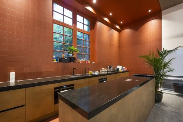 Moderne keuken met donker aanrechtblad, grote ramen en terracottakleurige wandtegels in een ruimte aan de Overtoom.