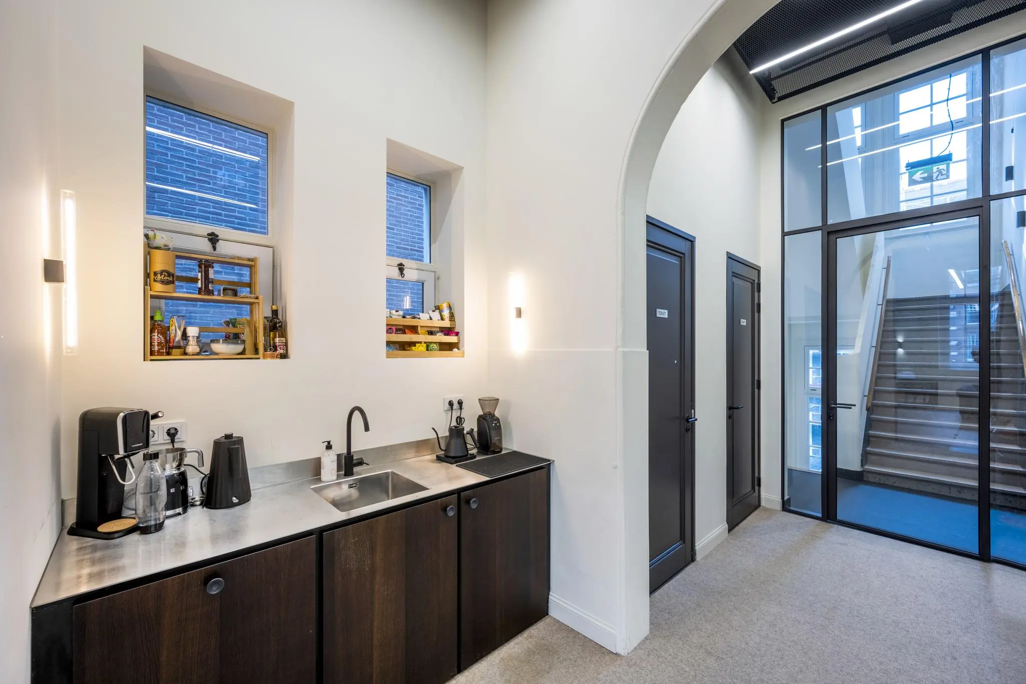 Moderne pantry met koffiemachine en spoelbak in een lichte gang bij trappenhuis in gebouw aan de Overtoom.