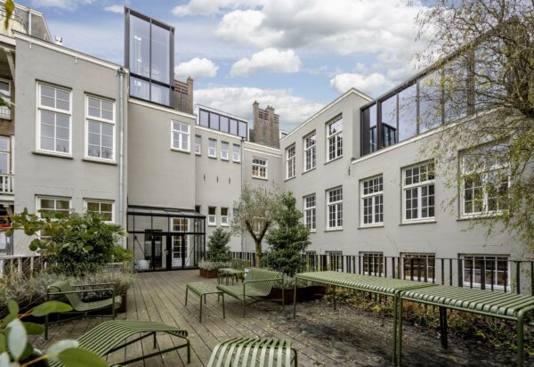 Binnenplaats met houten vlonder, groene zitbanken en planten, omringd door een lichtgrijs gebouw aan de Overtoom.