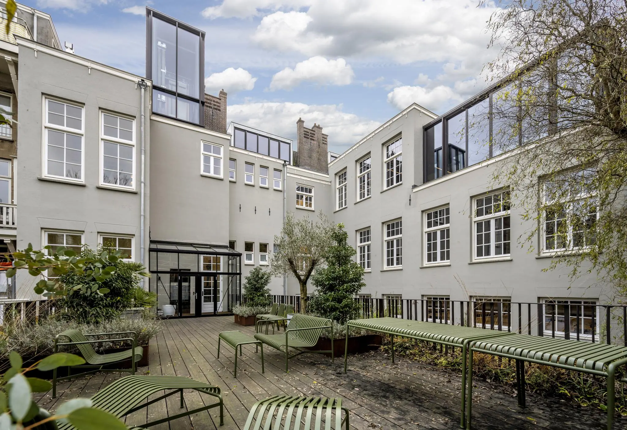 Binnenplaats met houten vlonder, groene zitbanken en planten, omringd door een lichtgrijs gebouw aan de Overtoom.