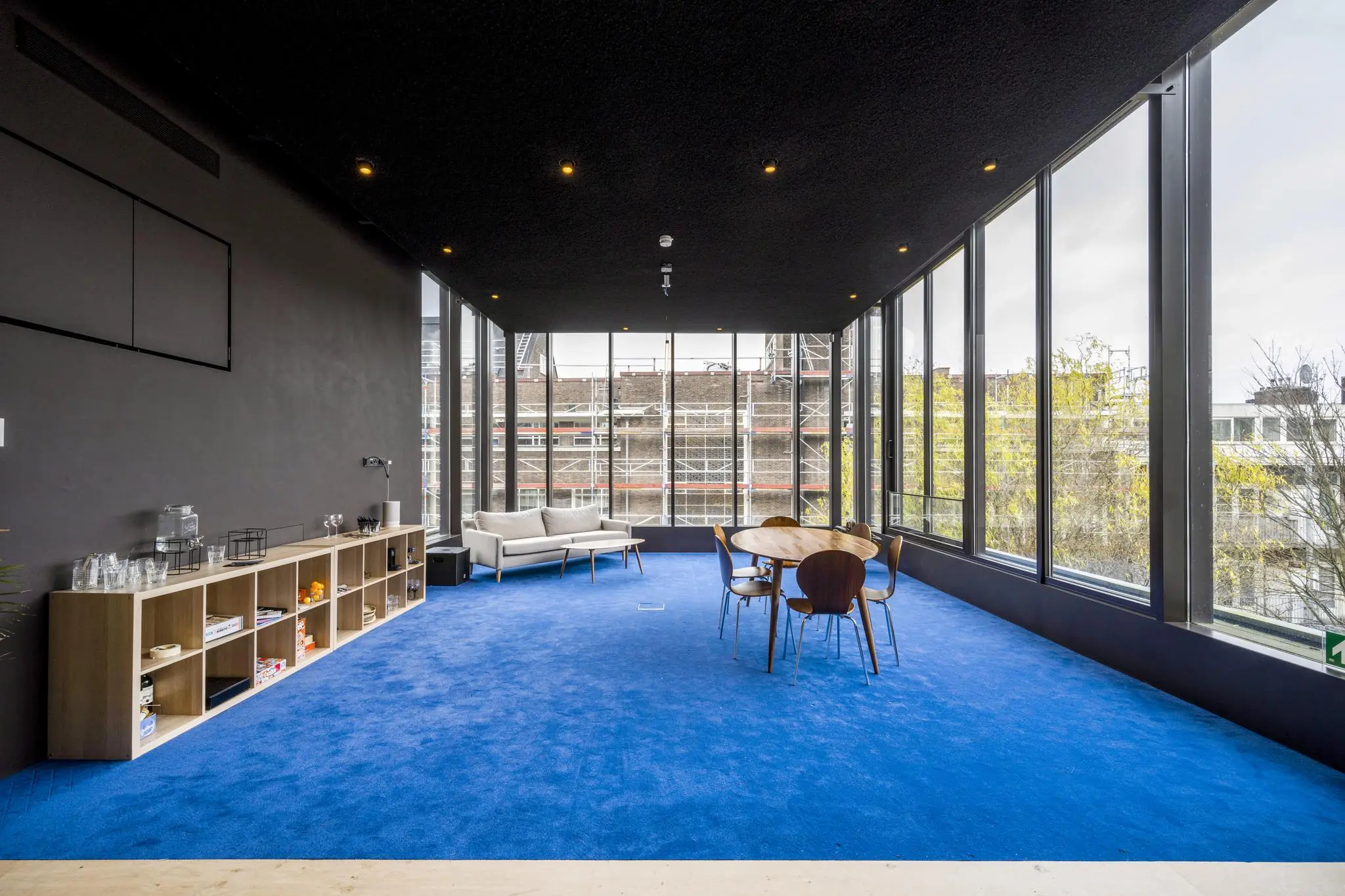 Moderne vergaderruimte aan de Overtoom met blauwe vloerbedekking, grote ramen en uitzicht op een gebouw in de steigers.
