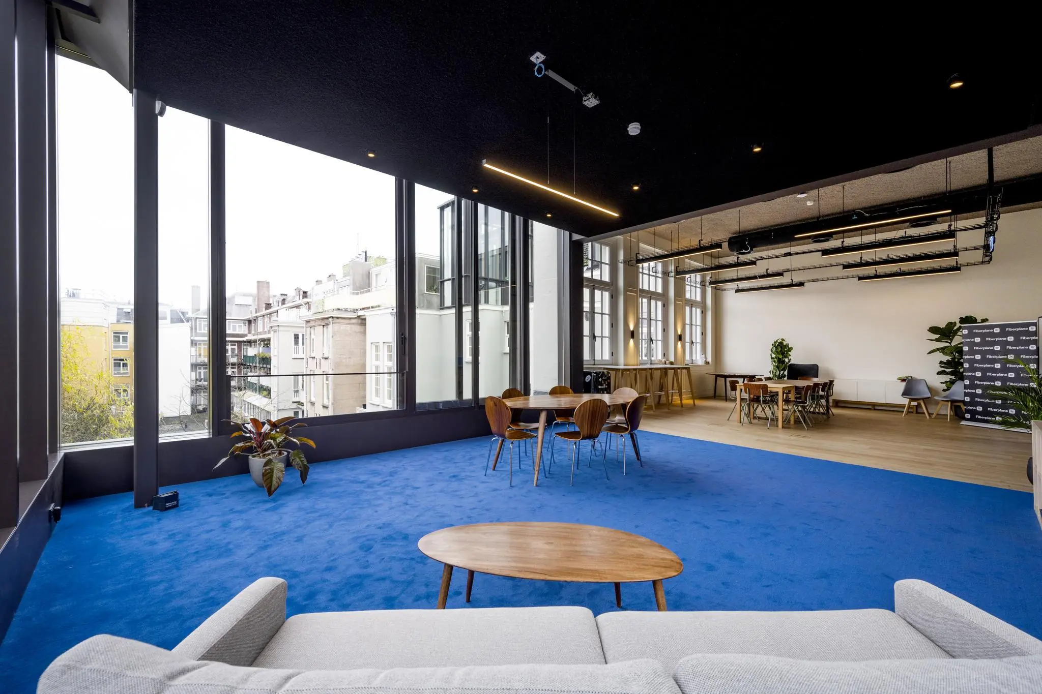 Modern ingerichte kantoorruimte aan de Overtoom met grote ramen, blauwe vloerbedekking en houten meubilair.