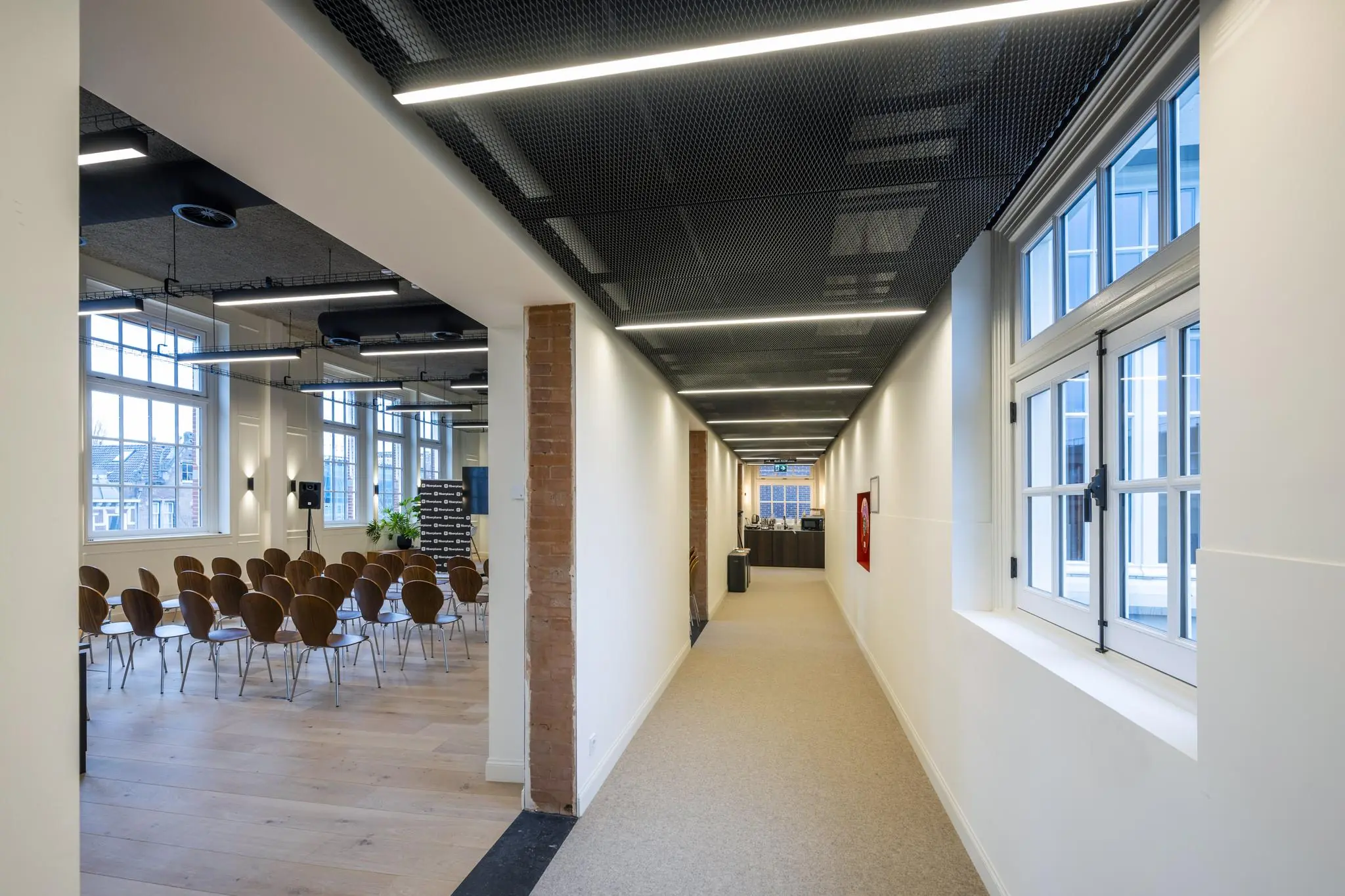 Moderne gang met uitzicht op een vergaderruimte met houten stoelen en grote ramen aan de Overtoom.