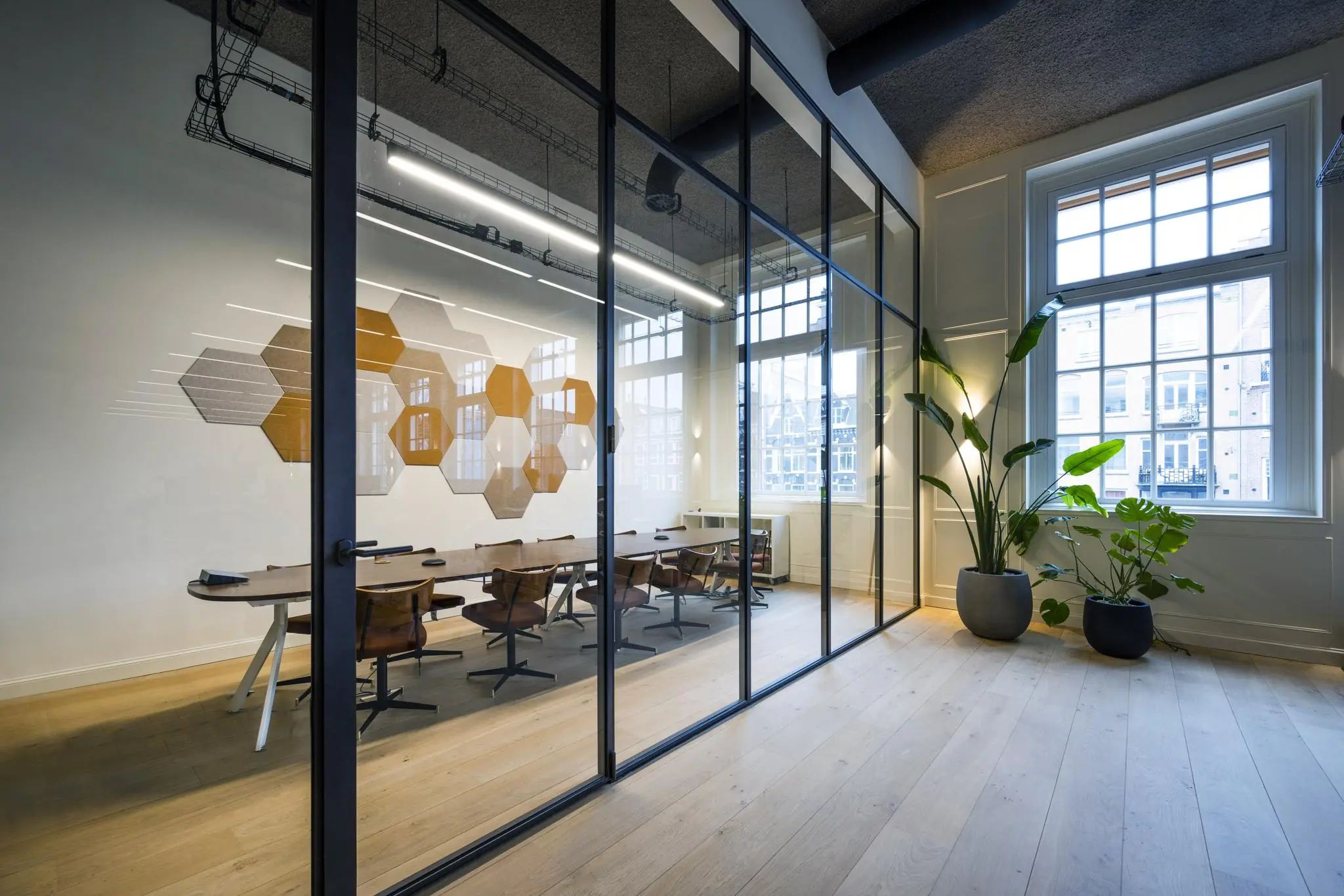 Moderne vergaderruimte aan de Overtoom met glazen wanden, houten vloer, designstoelen en muurdecoratie met hexagonale panelen.